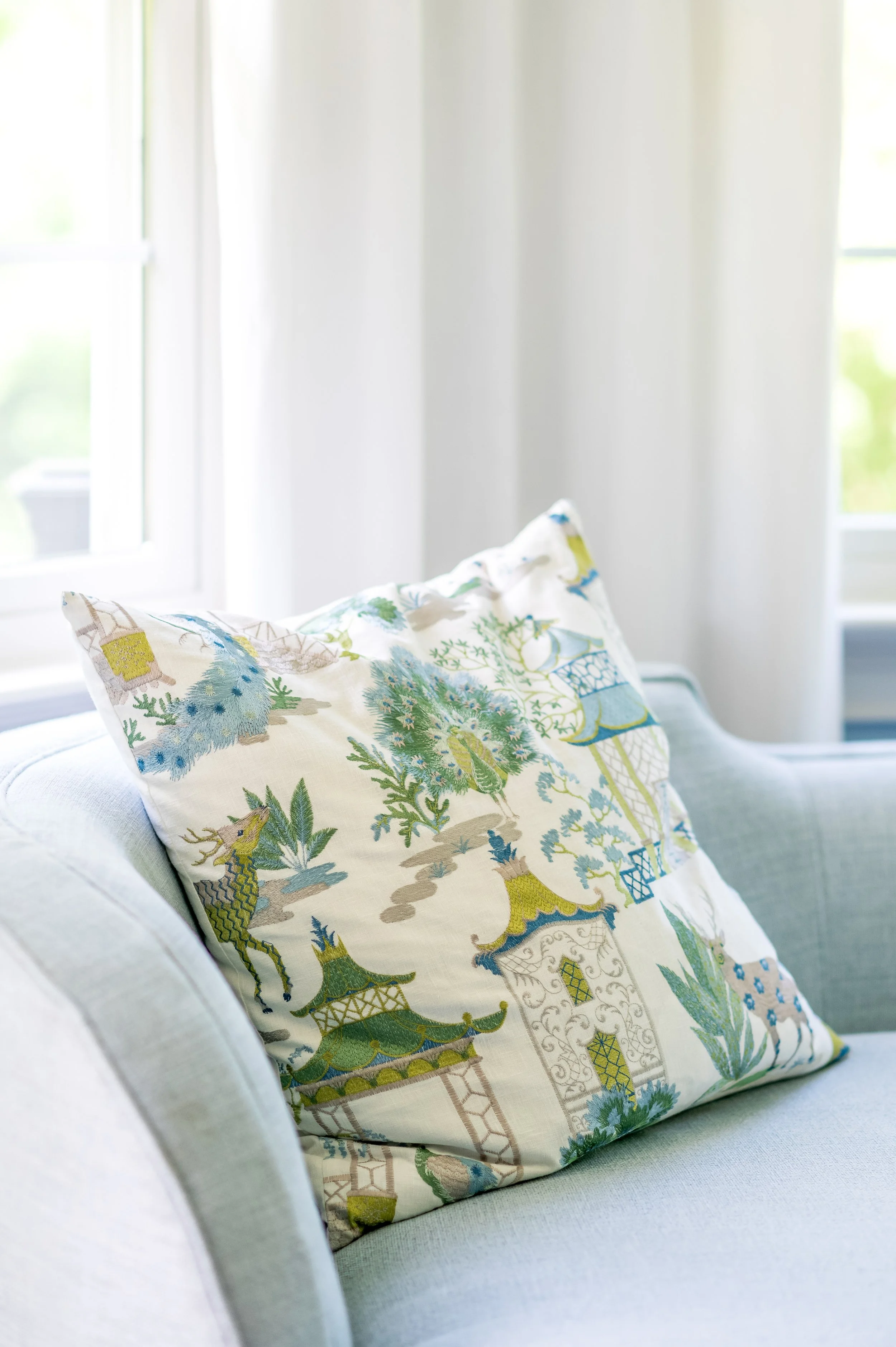 Decorative pillow with Asian-inspired design on a light-colored sofa near a window.