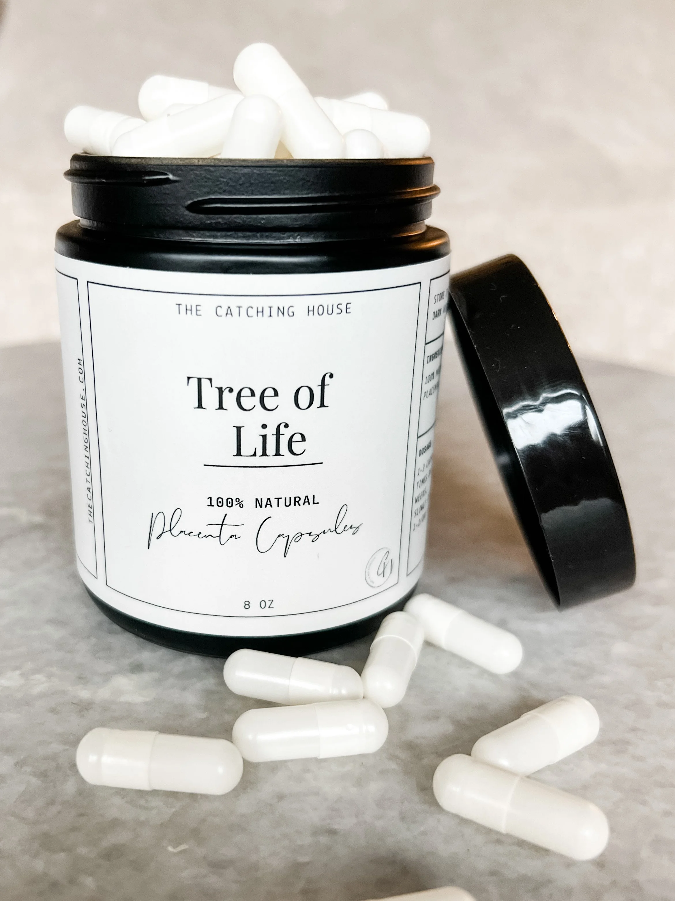 A black jar labeled 'Tree of Life' containing white capsules with some capsules spilled on a light grey surface.