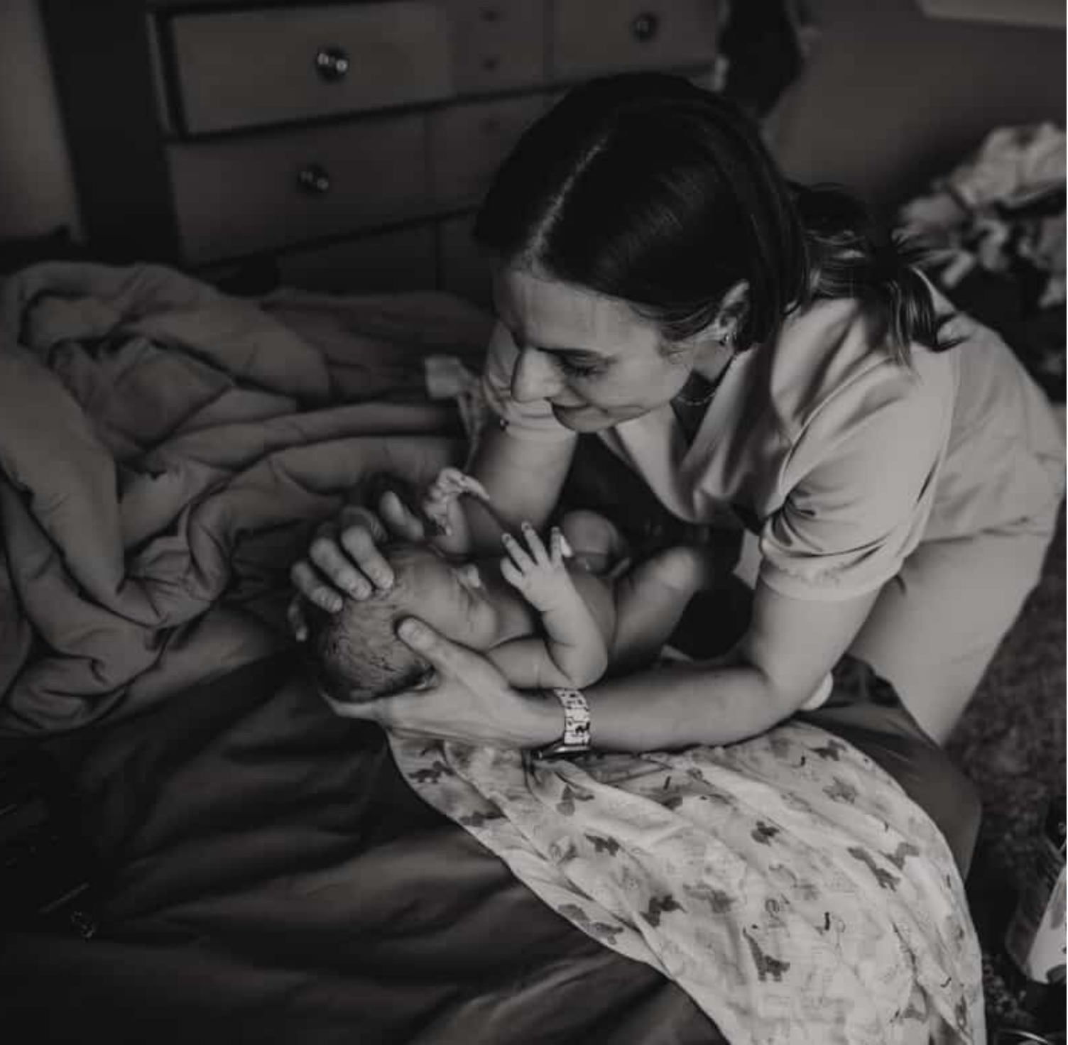 Midwife Andrea Durham from The Catching House, holding a newborn baby in her arms, looking at the baby supportively.