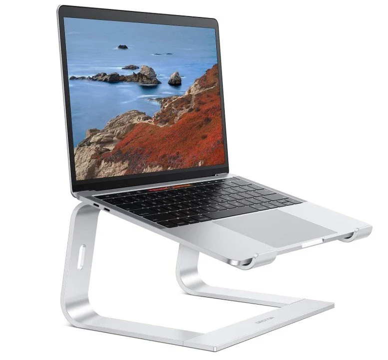 Silver laptop on a stand with a coastal landscape on the screen, showing rocky cliffs and the ocean.
