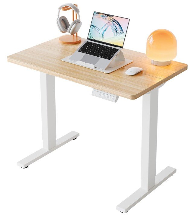 Photo of a wooden desk with a laptop, white mouse, headphones on a stand, and a round orange lamp.