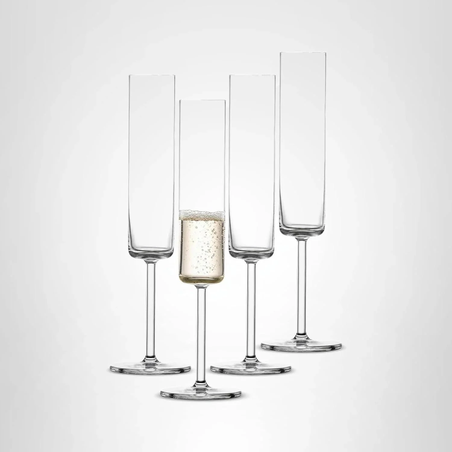 Four empty champagne flutes, one with champagne, on a plain background.