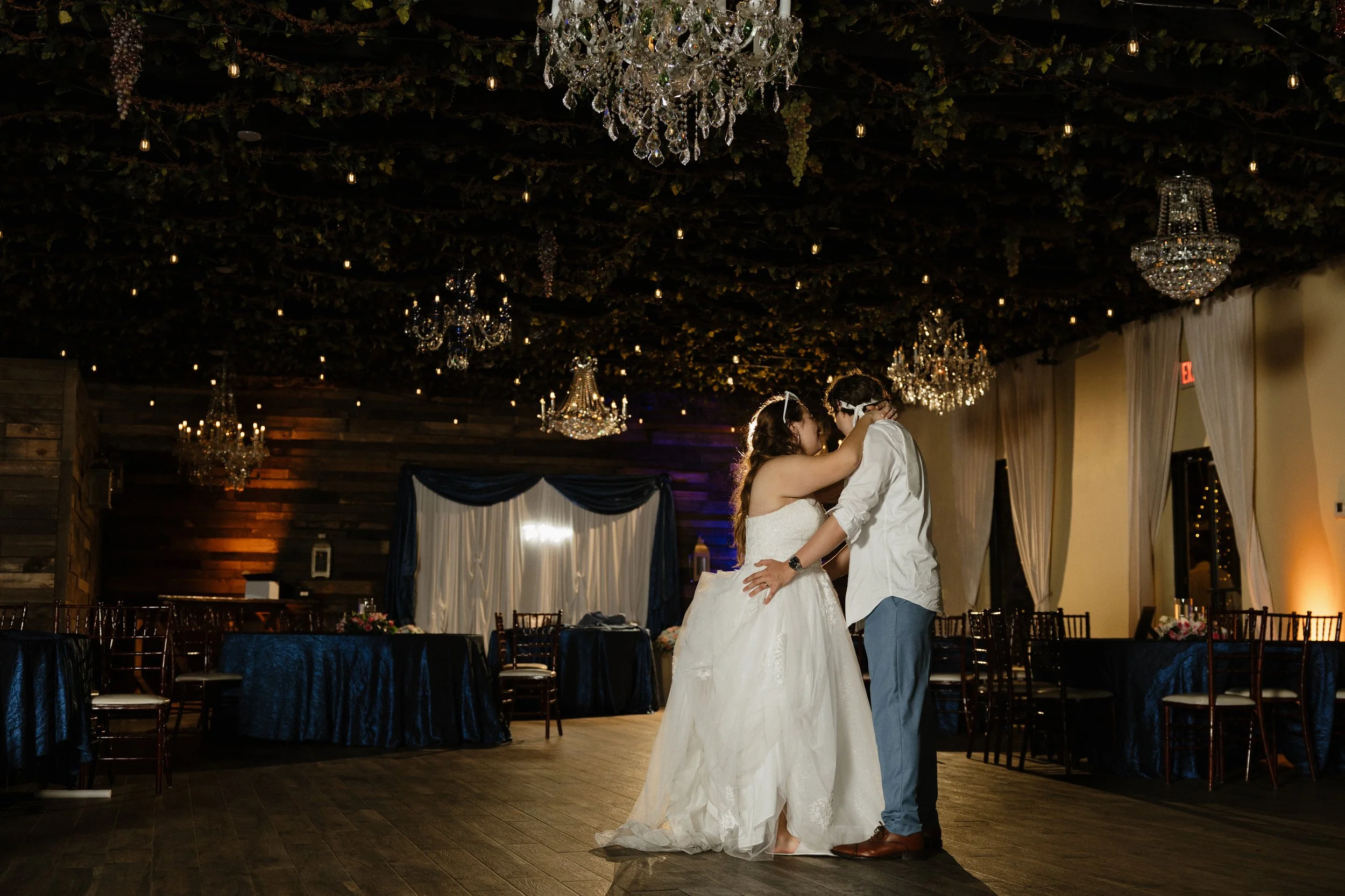A bride and groom sharing a dance at their wedding reception, with chandeliers hanging from a decorated ceiling.