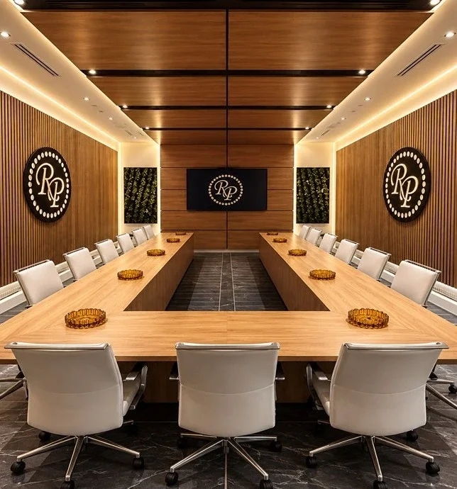 Custom Rocky Patel conference room by Domina Design featuring a bespoke wood conference table, architectural wall panels, integrated lighting, and branded interior details.