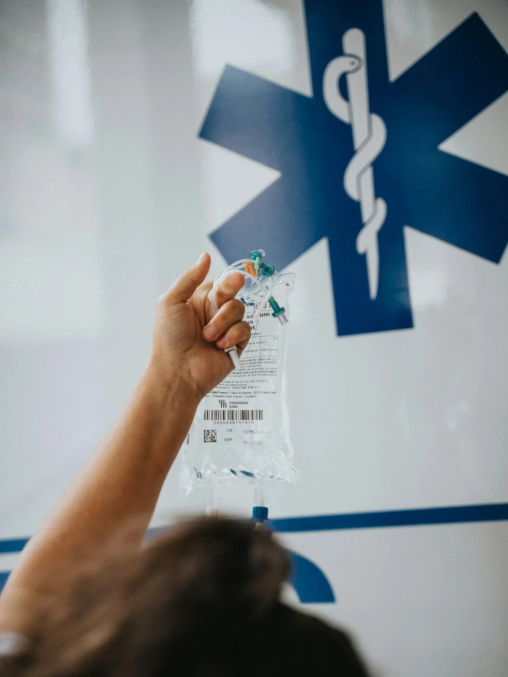A paramedic holds an IV bag next to an ambulance