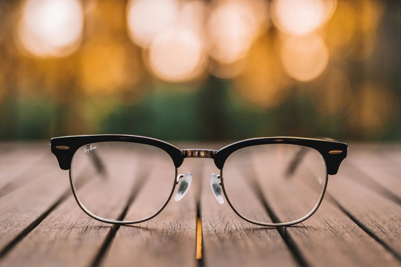 A pair of black and silver Ray-Ban glasses on a wooden surface with a blurred, glowing background.
