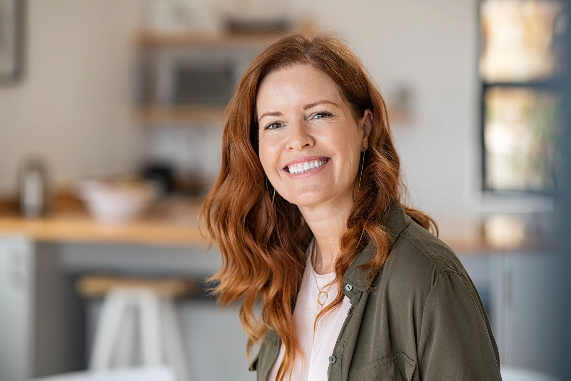 Smiling woman with long, wavy red hair in a kitchen.