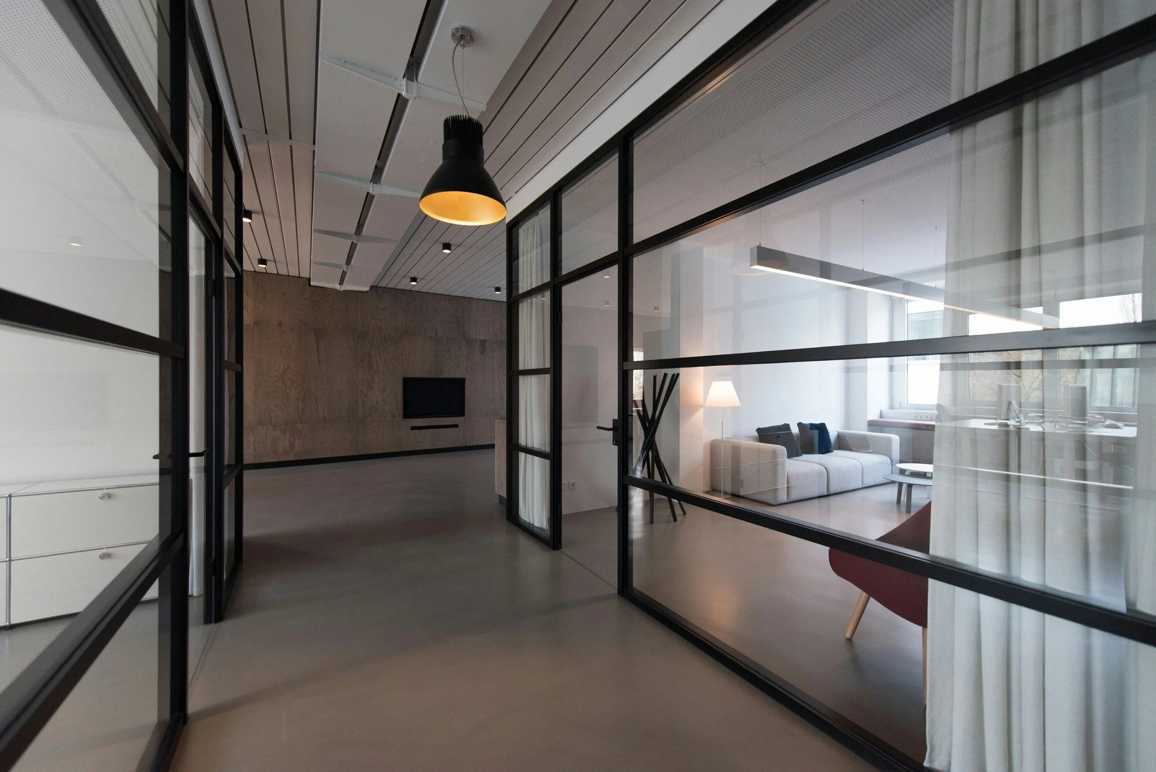 Modern apartment interior with glass walls, white sofa, black cushions, and a floor lamp with white shade.
