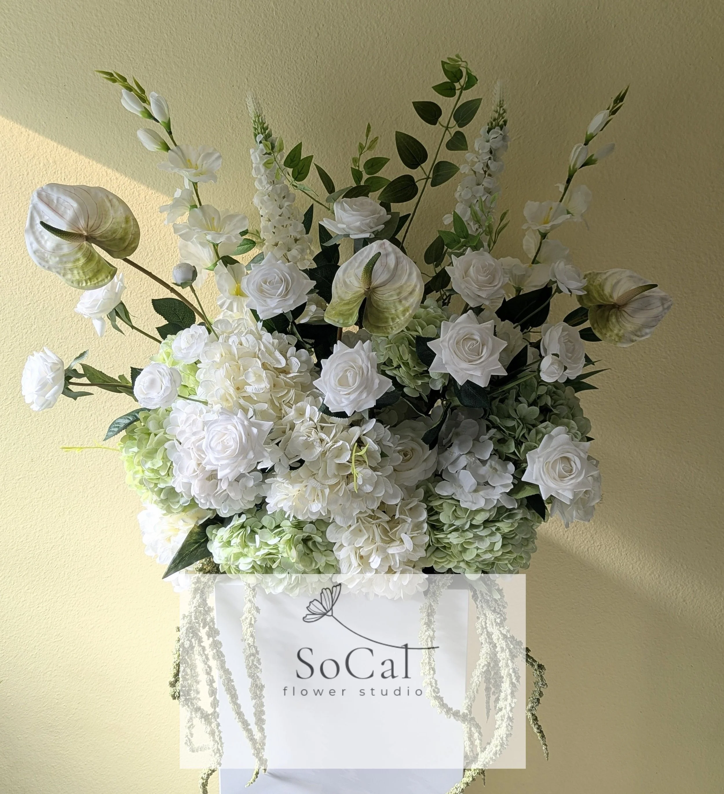Arrangement of white flowers including roses, hydrangeas, and other blooms in a black vase on a white pedestal