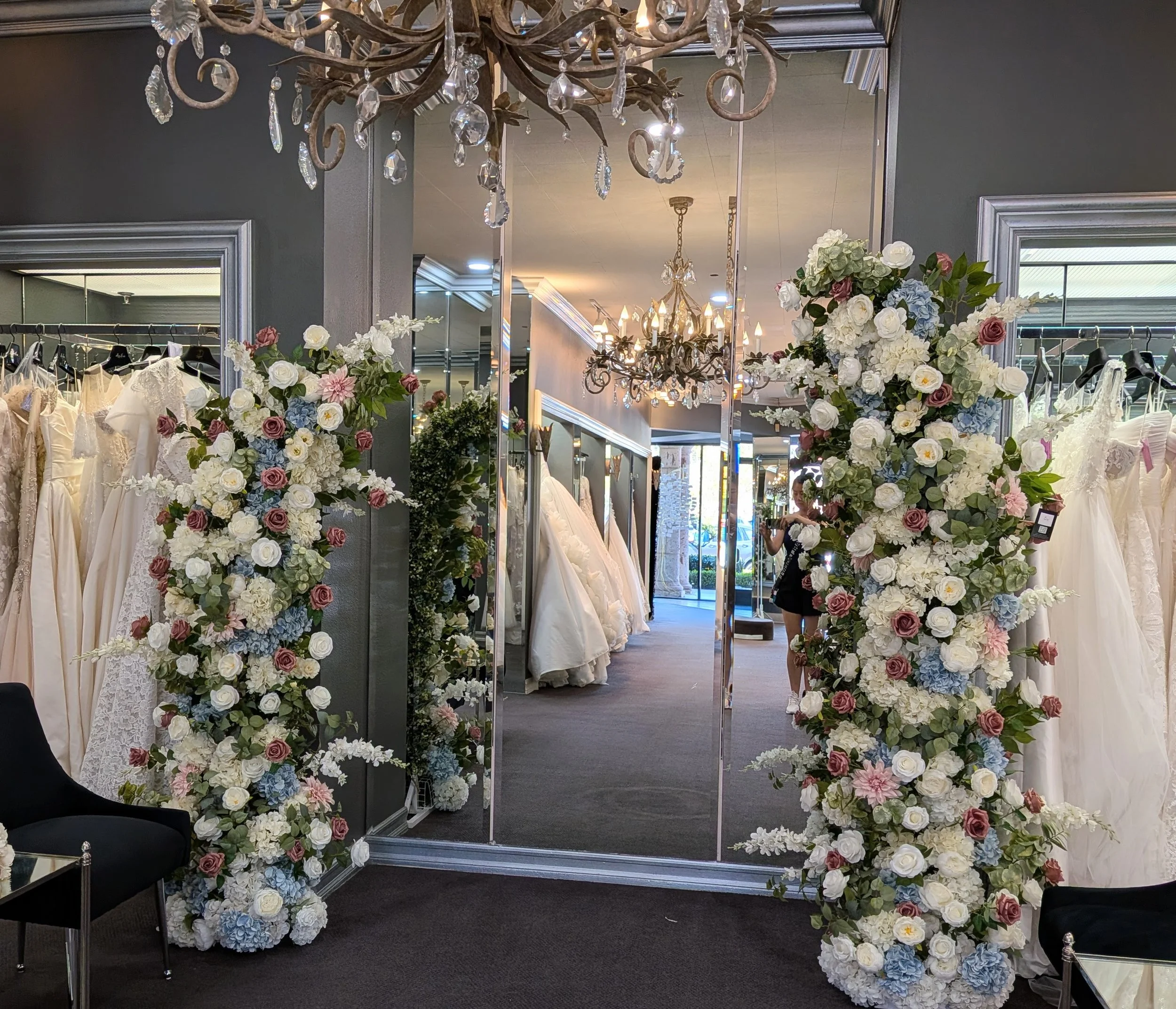 Two large floral archways with pink, peach, white, and blue flowers, flanking a tall mirror with gold trim and Eiffel Tower decoration, at a wedding venue.