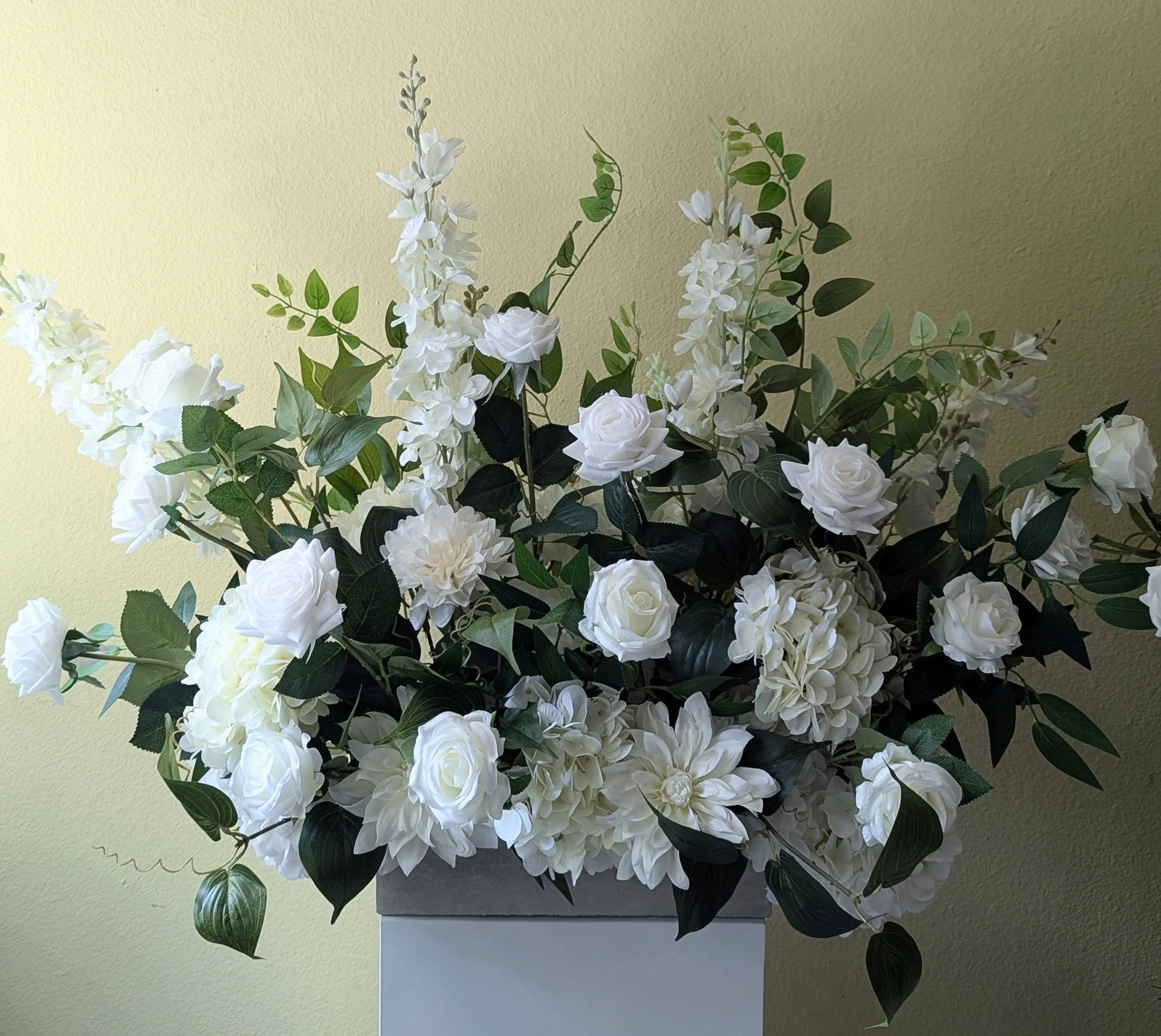 White aisle arrangement made of roses and other flowers in a garden with green bushes and trees.