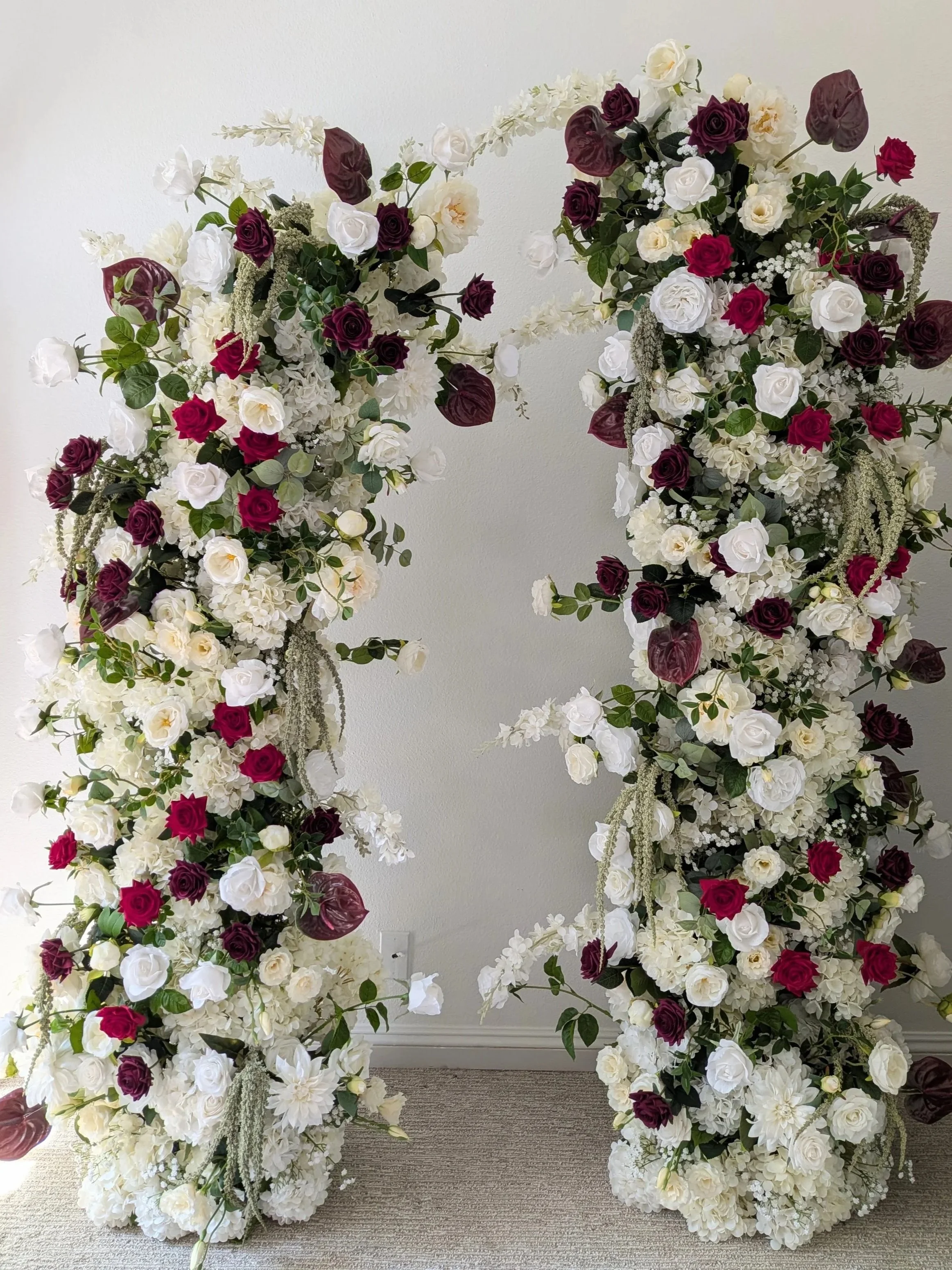Large floral display with white, cream, and deep red roses, along with greenery, arranged in cascading clusters.