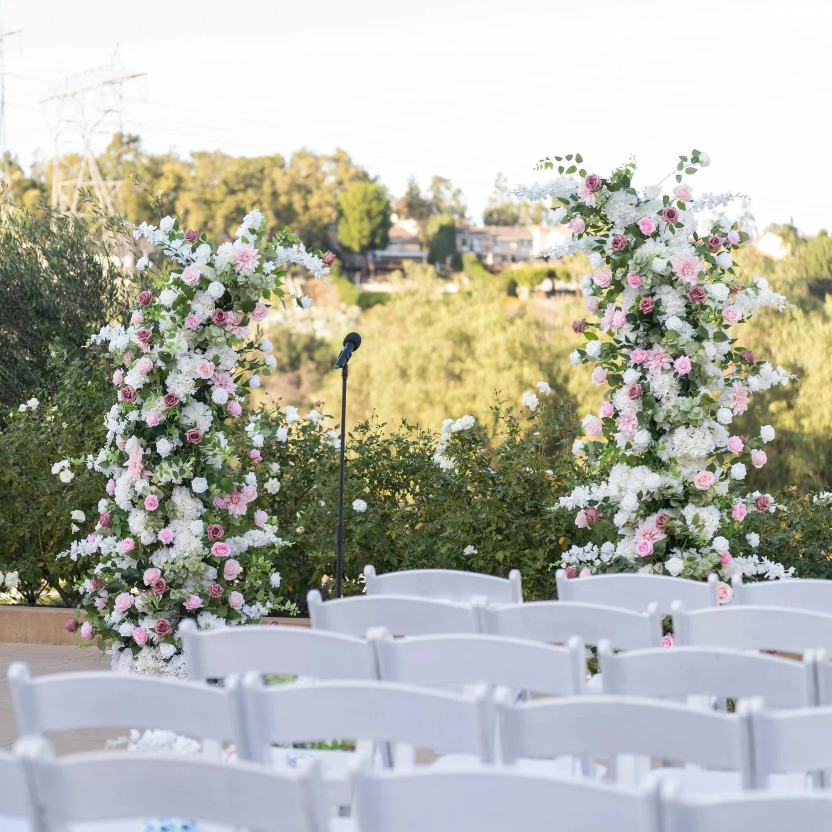 Beautiful floral wedding arch with pink, white, and burgundy roses and green foliage on a grassy outdoor setting.