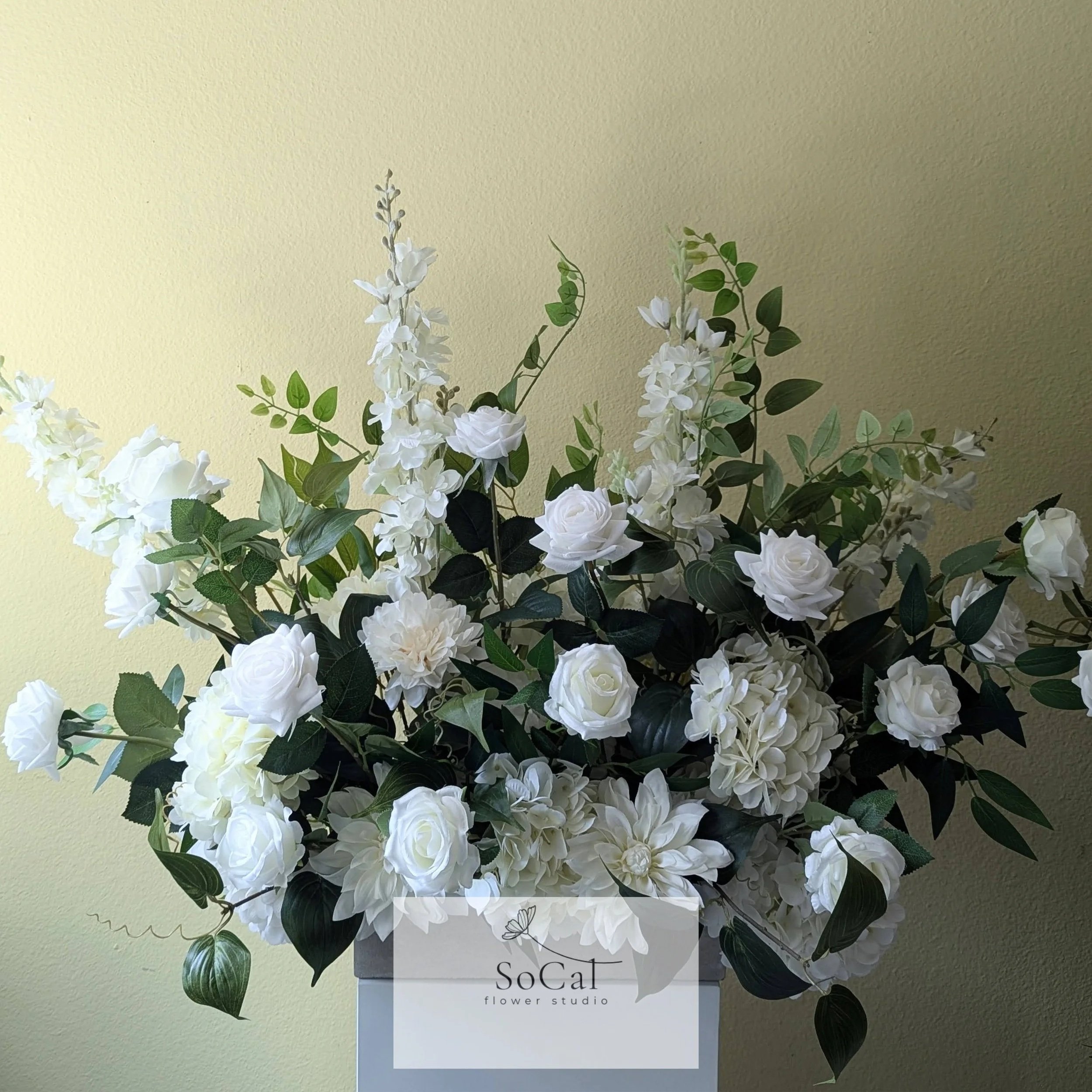 White aisle arrangement made of roses and other flowers in a garden with green bushes and trees.