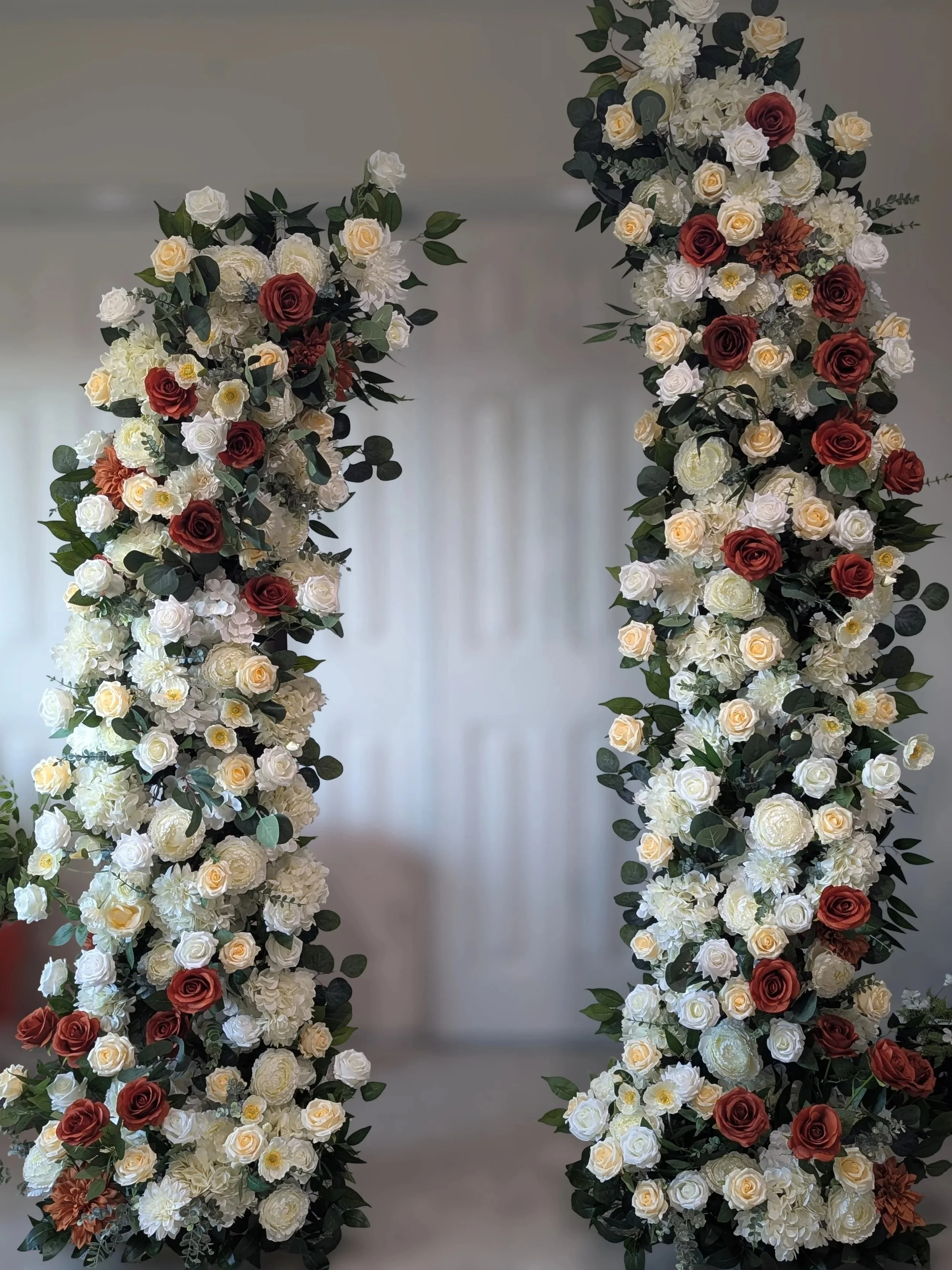 A floral wedding arch made of white, peach, and light pink roses in an outdoor garden setting.