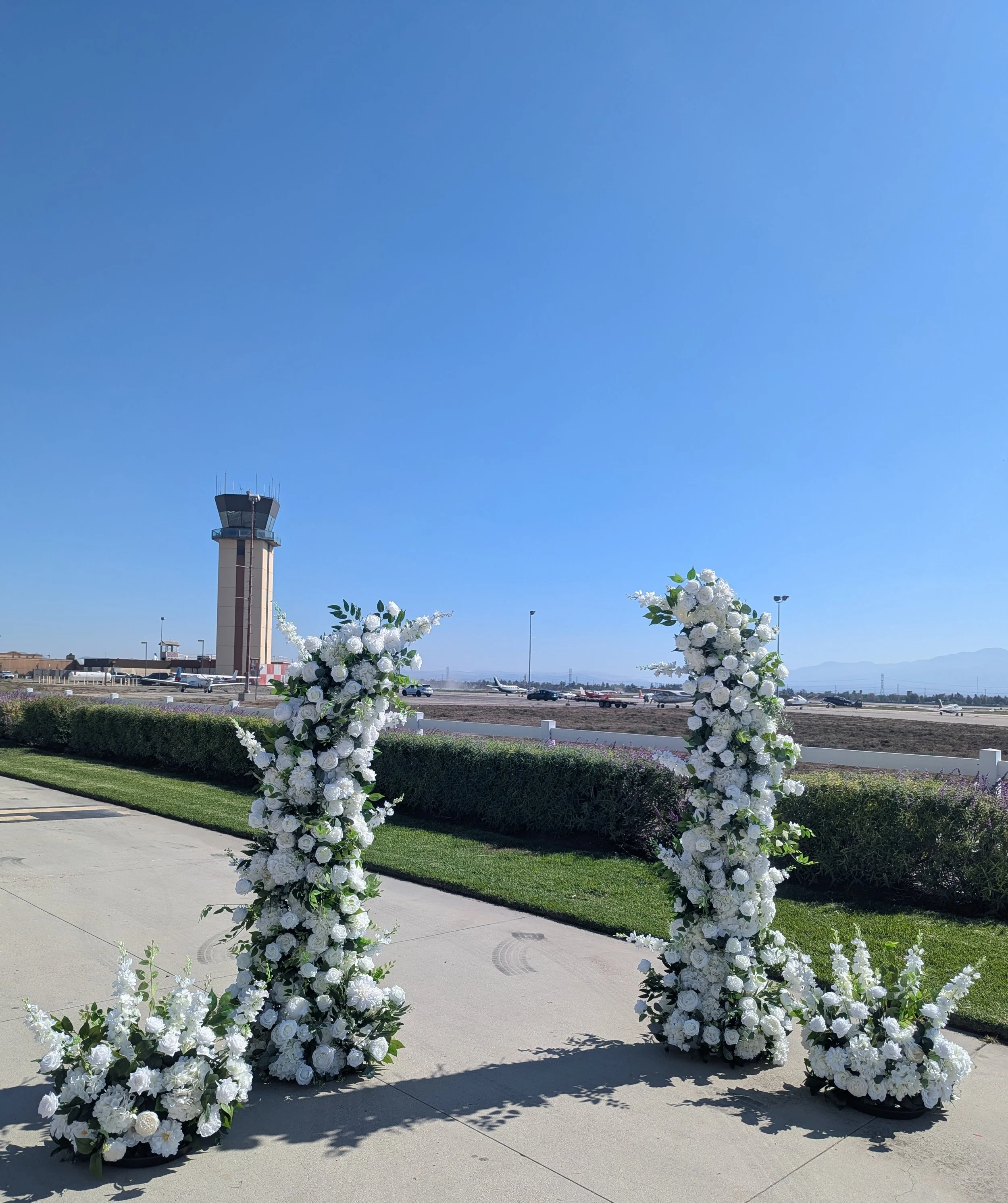 White floral wedding arch at an airport with control tower and runway in the background.