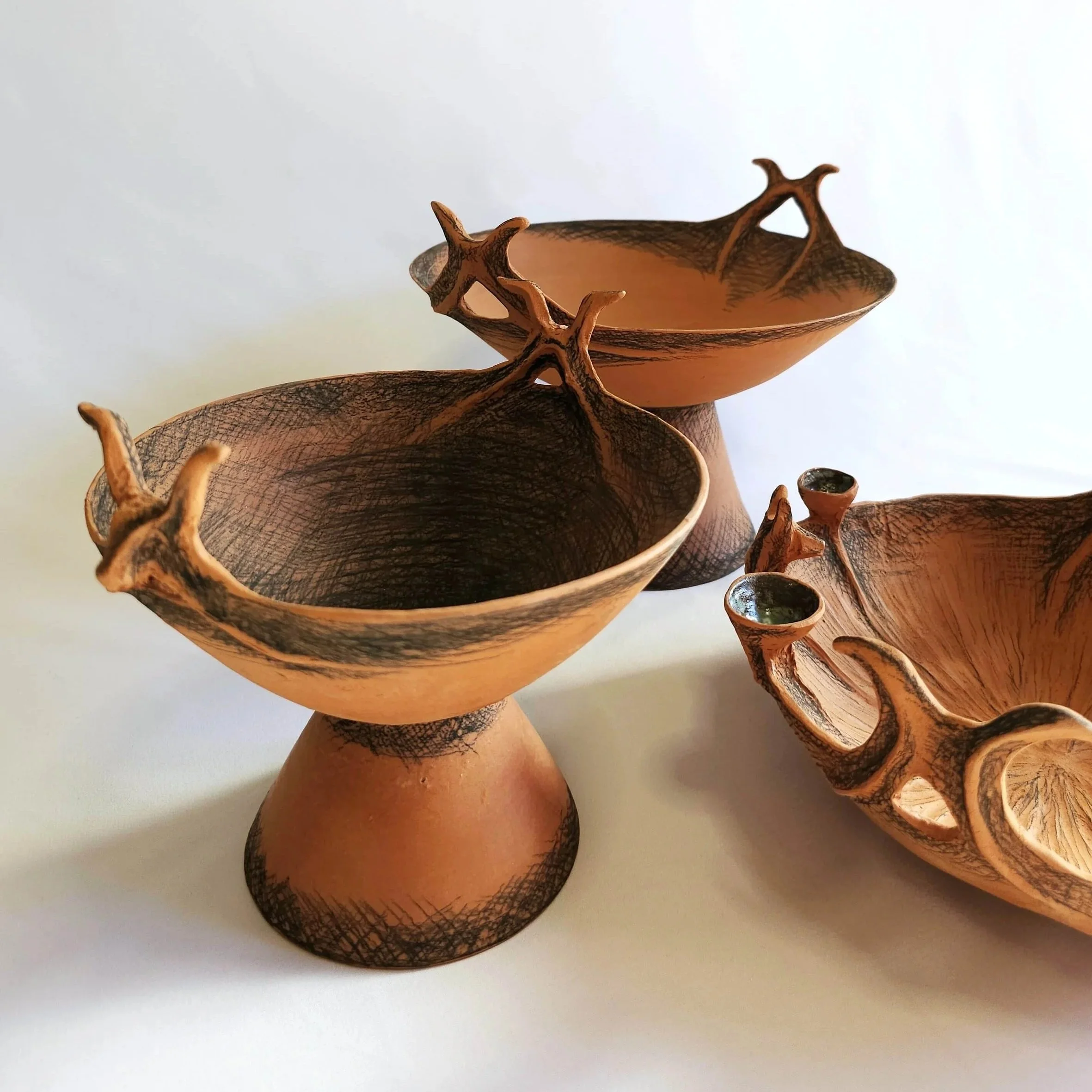 Three hand-built terracotta vessels inspired by ancient Greek pottery, decorated with black underglaze pencil