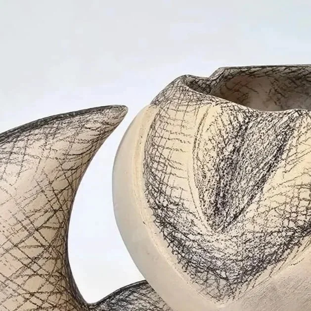 Close-up of two abstract ceramic sculptures with textured black markings on a white surface.