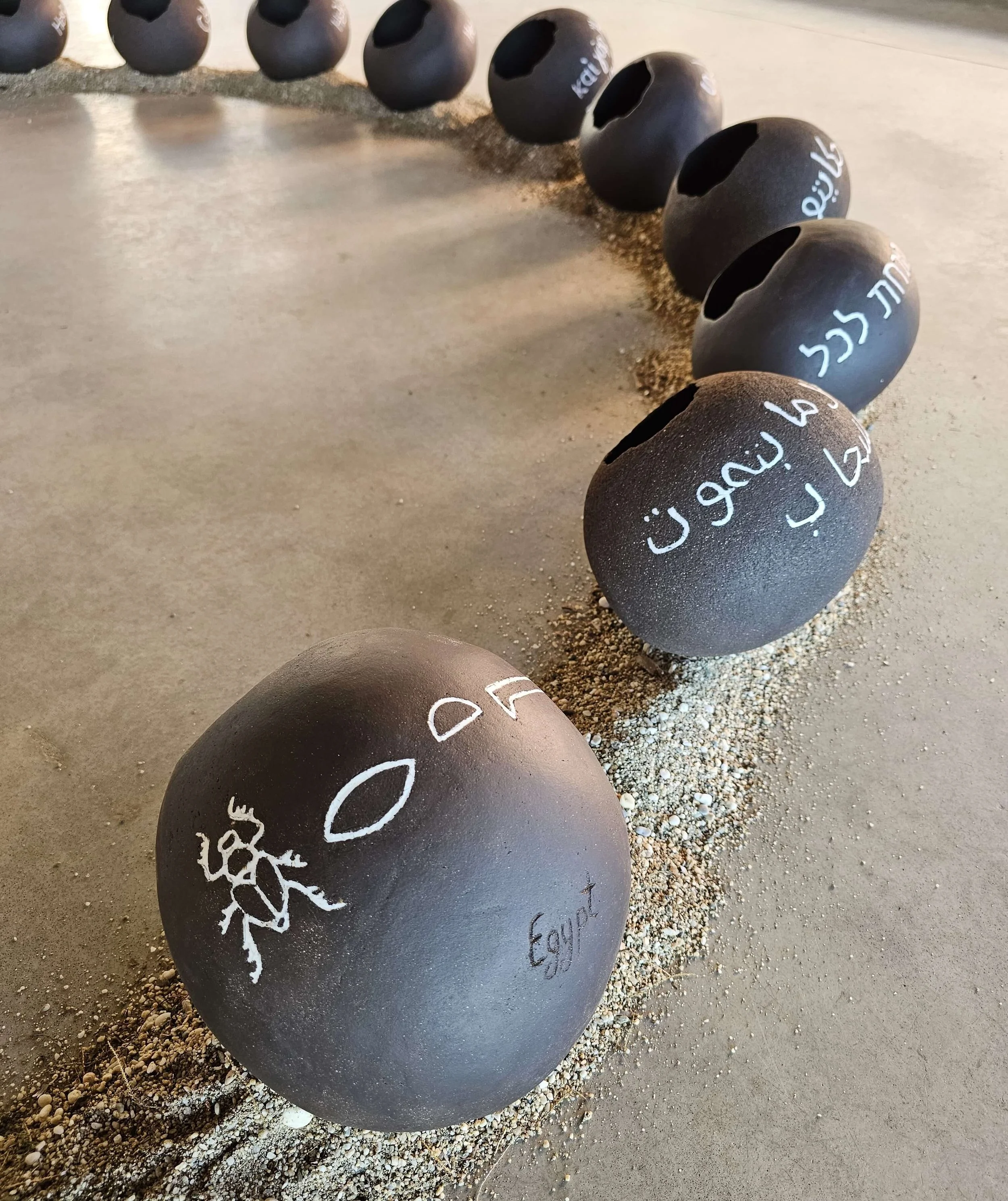 Black spherical stones with white chalk-like drawings and writings on a gravelly ground surface.