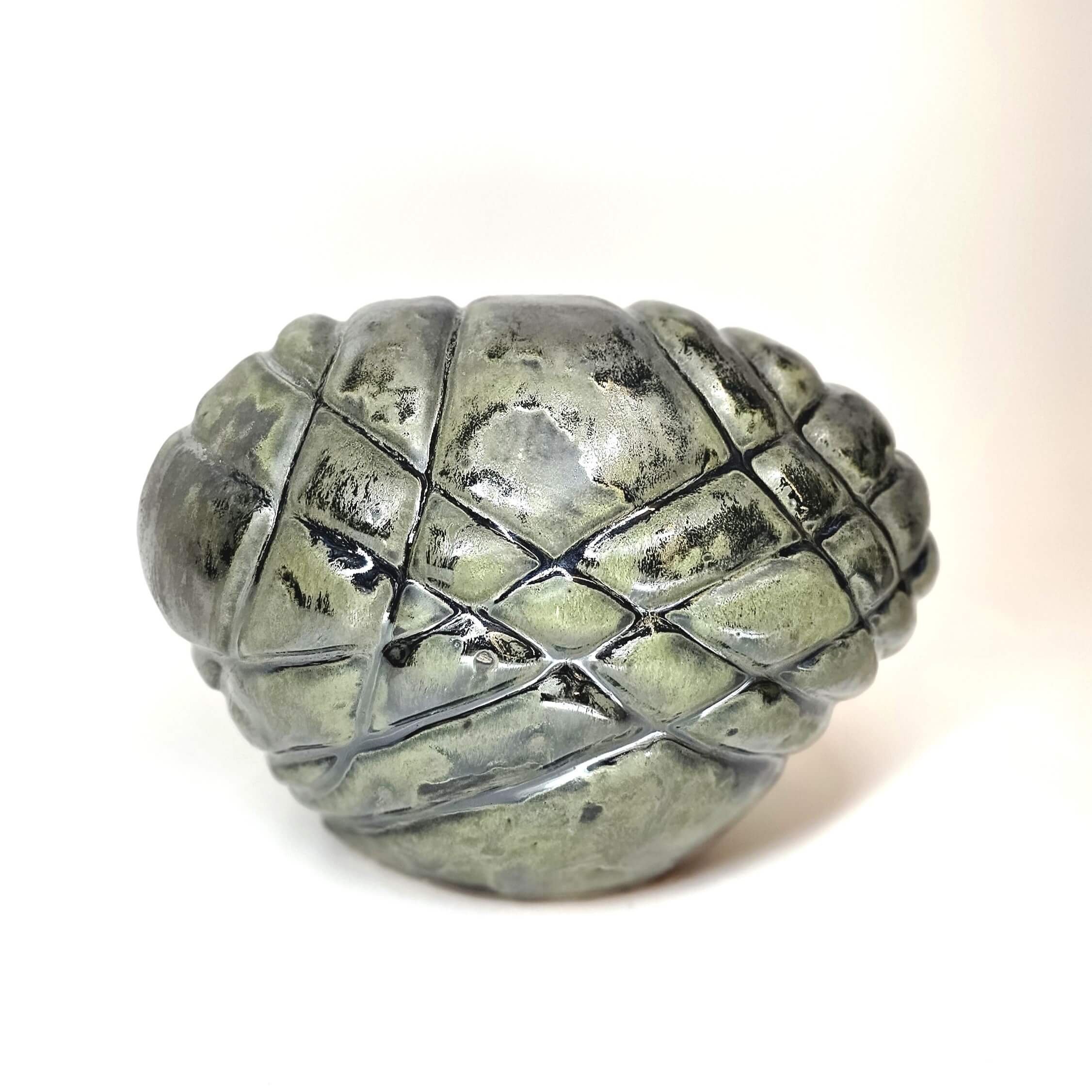 Mirsini Roumelioti. Mirsini Ceramics. Asphyxia. Hugs. Close-up of a metallic pine cone ornament with a shiny surface, set against a plain white background.