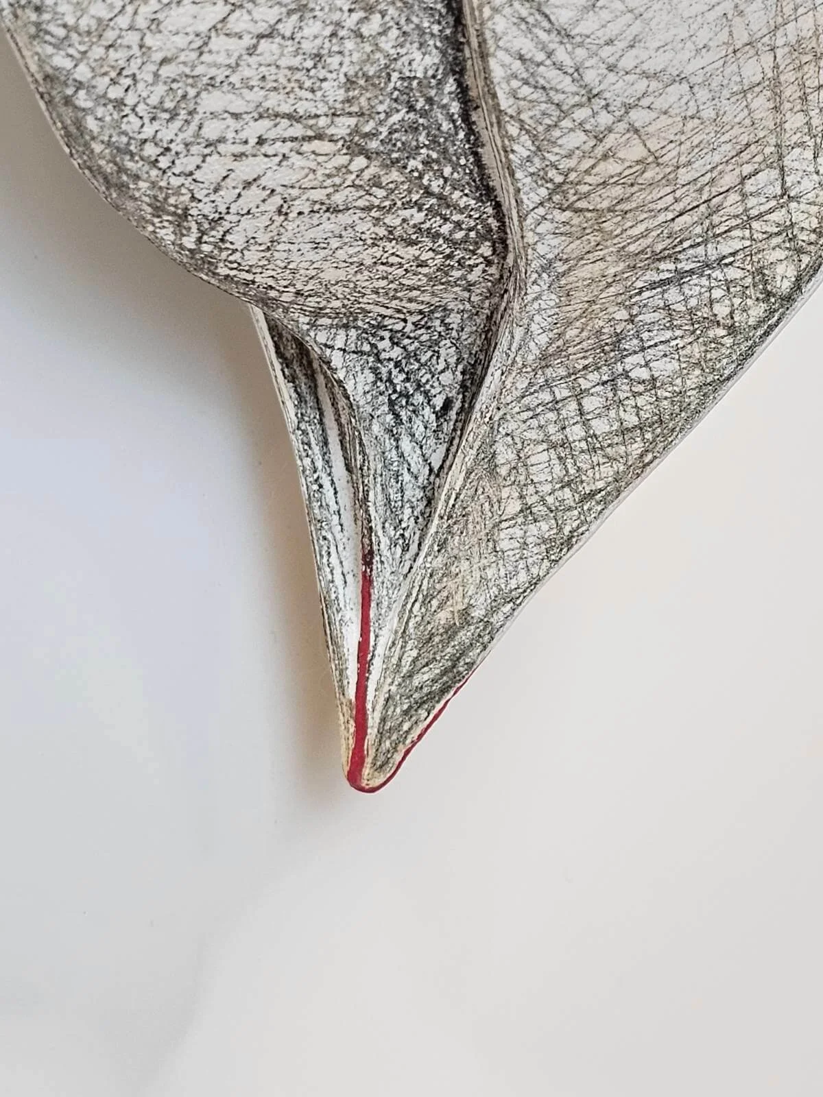 Close-up of an abstract sculpture with textured, cracked surface and pointed tip outlined in red, against a white background.