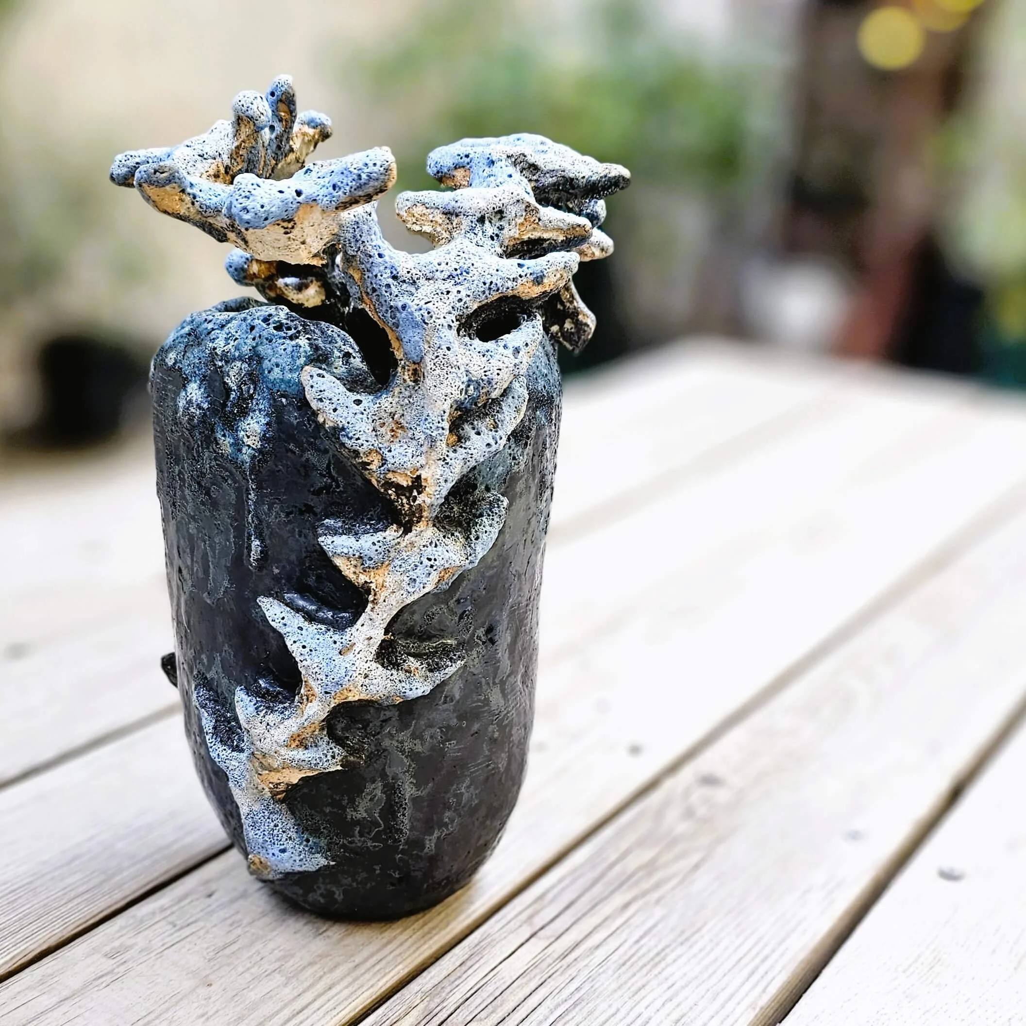 Mirsini Roumelioti. Mirsini Ceramics. Acanthus Reverie II. Ceramic vase shaped like a tree with foam and soap suds on top, placed on a wooden table outdoors.