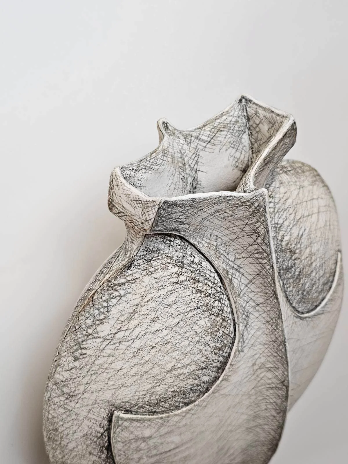 A white ceramic vase with a textured surface and a wavy, sculptural top edge.