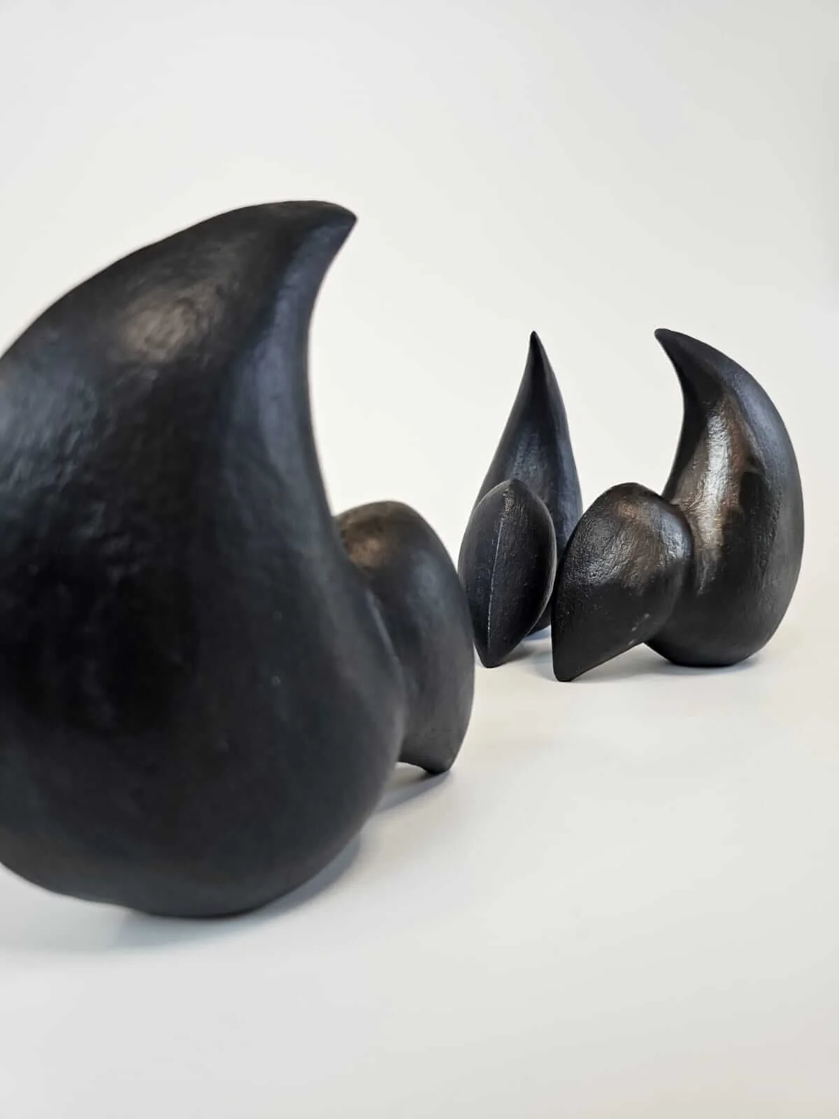 Close-up photograph of black ceramic sculptures with curved, abstract shapes placed on a white surface against a plain white background.