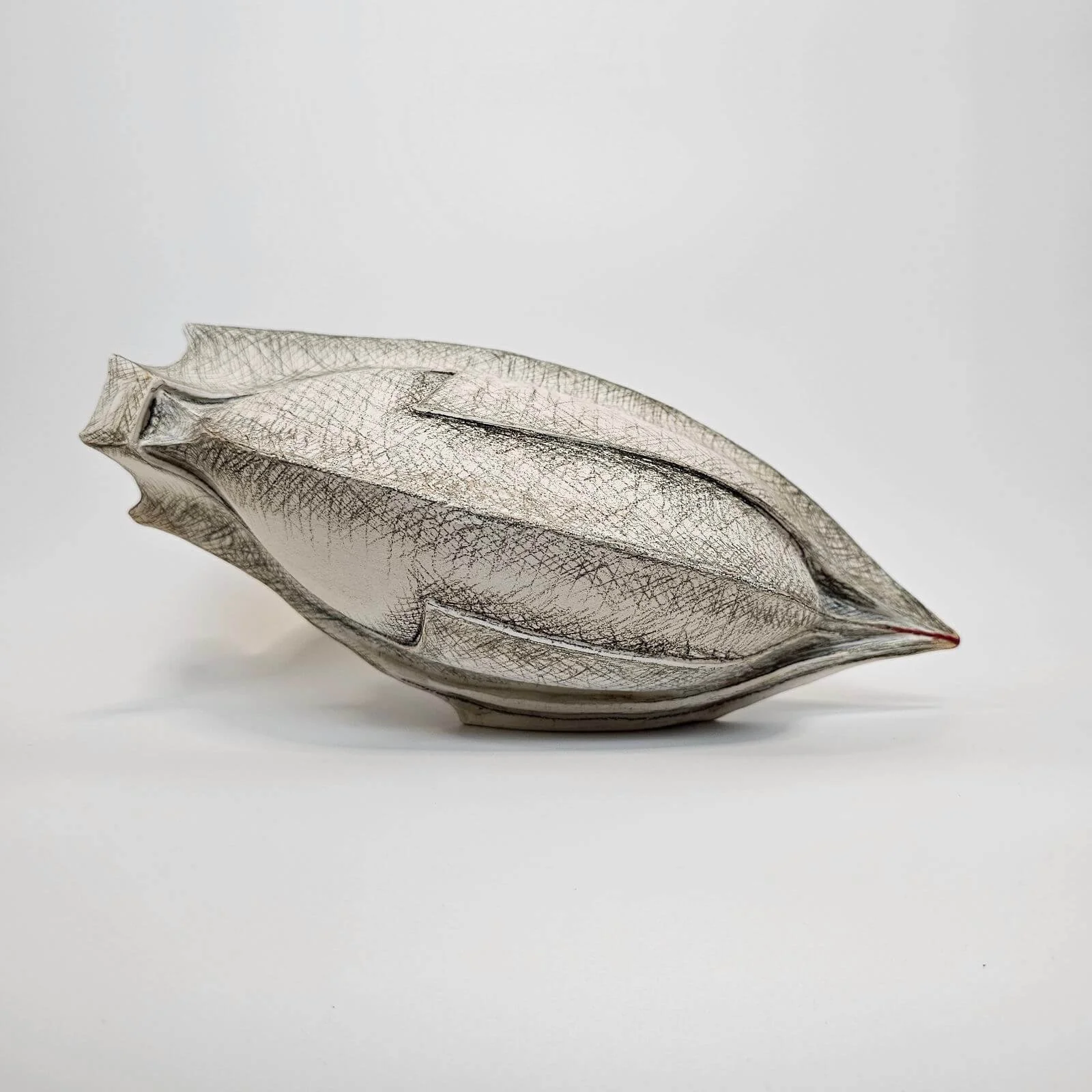 Decorative silver leaf-shaped object with intricate vein pattern against a plain white background.
