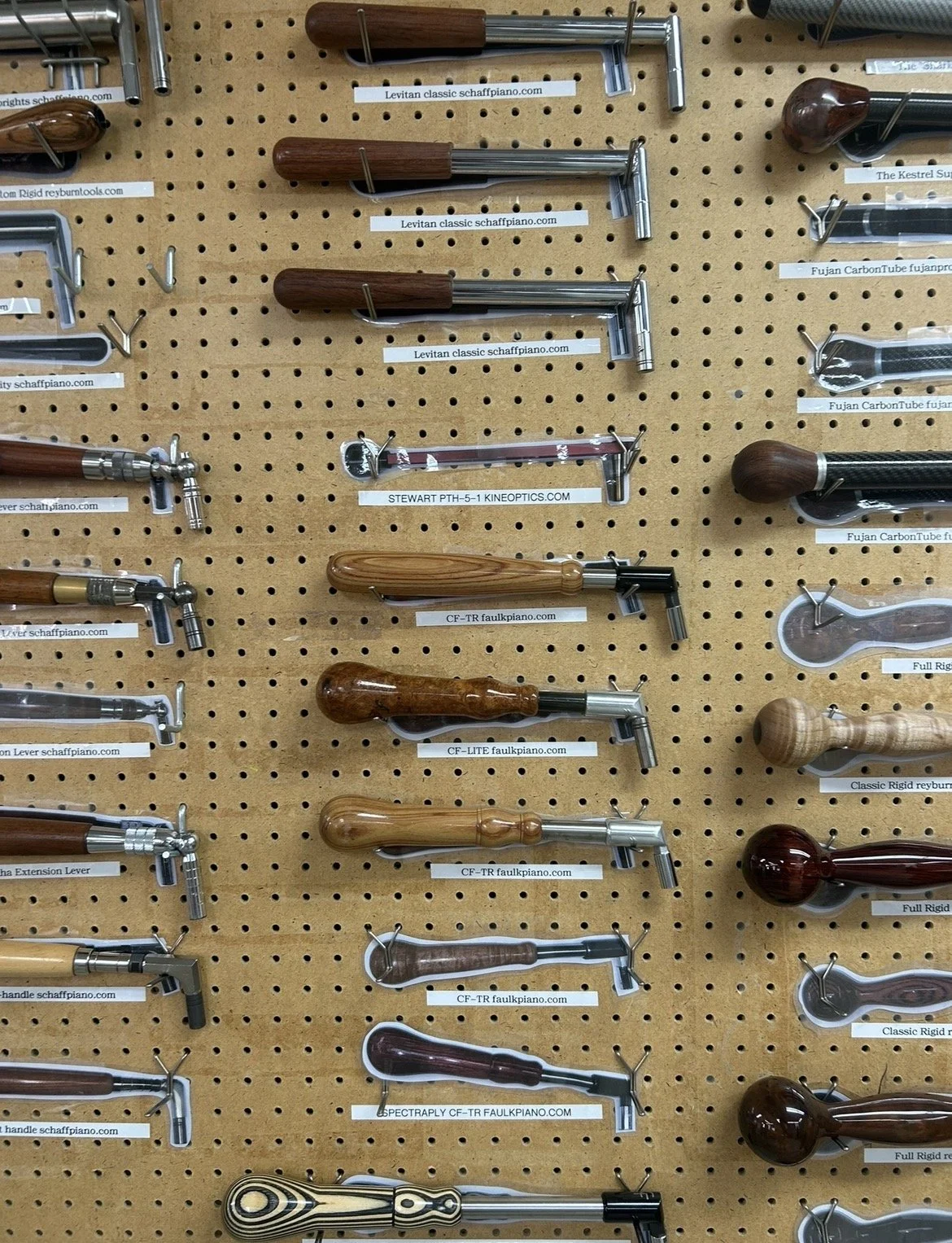A display wall with various piano action parts, including hammer shanks and tips, arranged on a perforated board with labels.