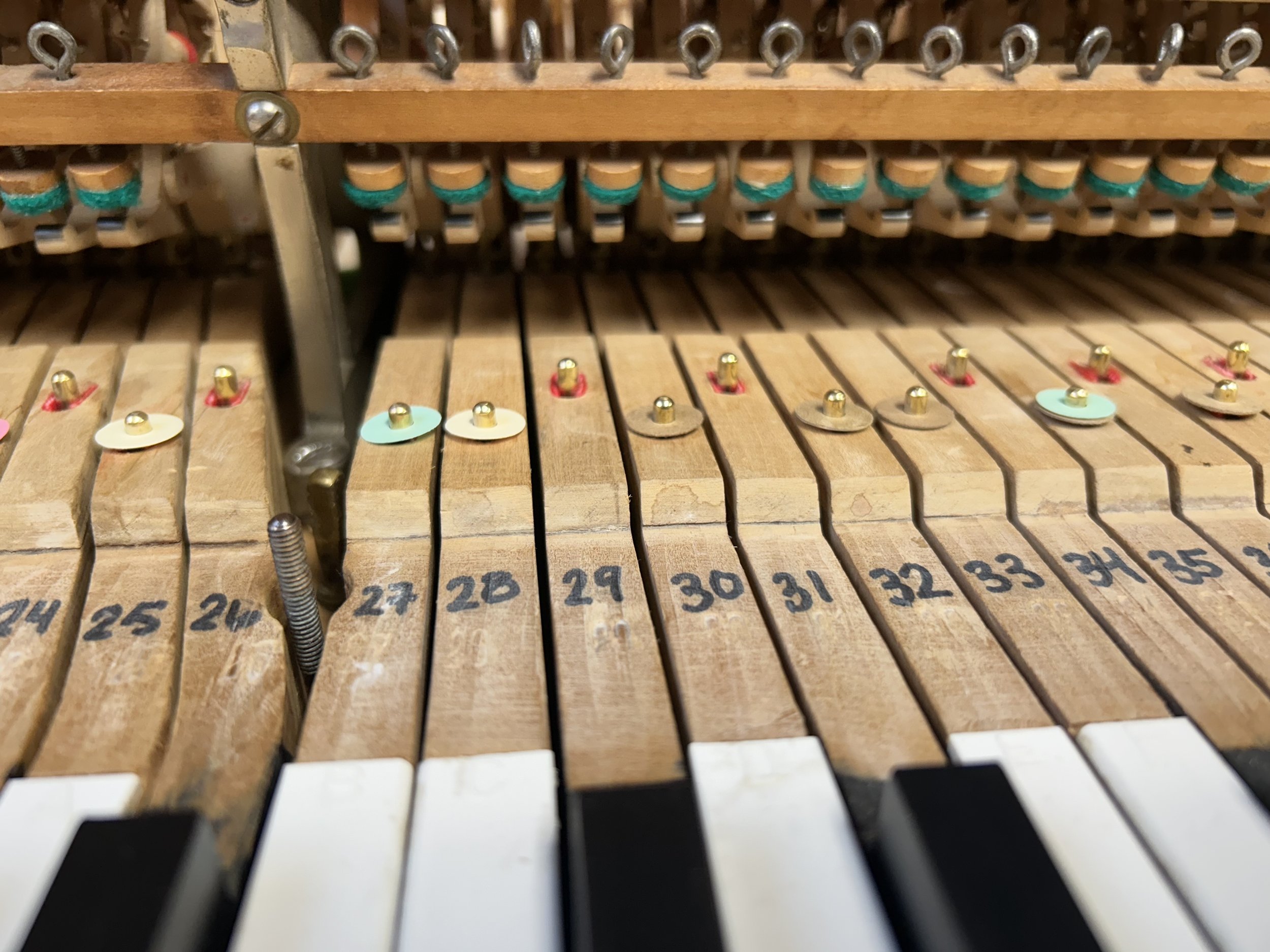 Close-up of the inside of an upright piano showing wooden hammers, metal strings, and black and white keys.