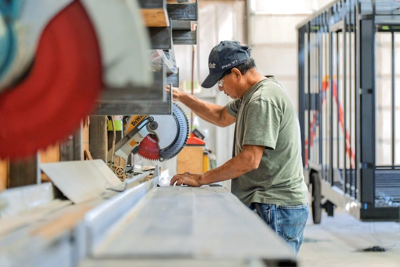 A man wearing a backwards baseball cap and glasses working with a circular saw in a workshop.