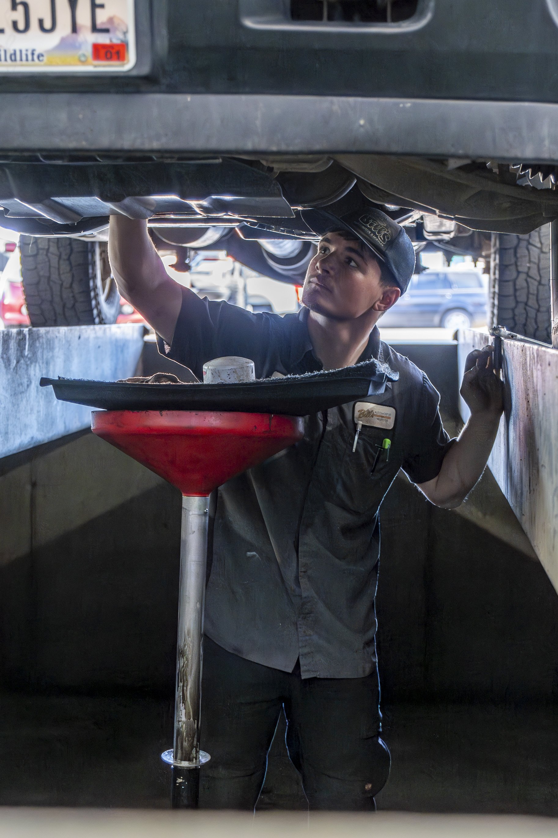 A mechanic working underneath a vehicle, inspecting or repairing its underside in a parking lot.