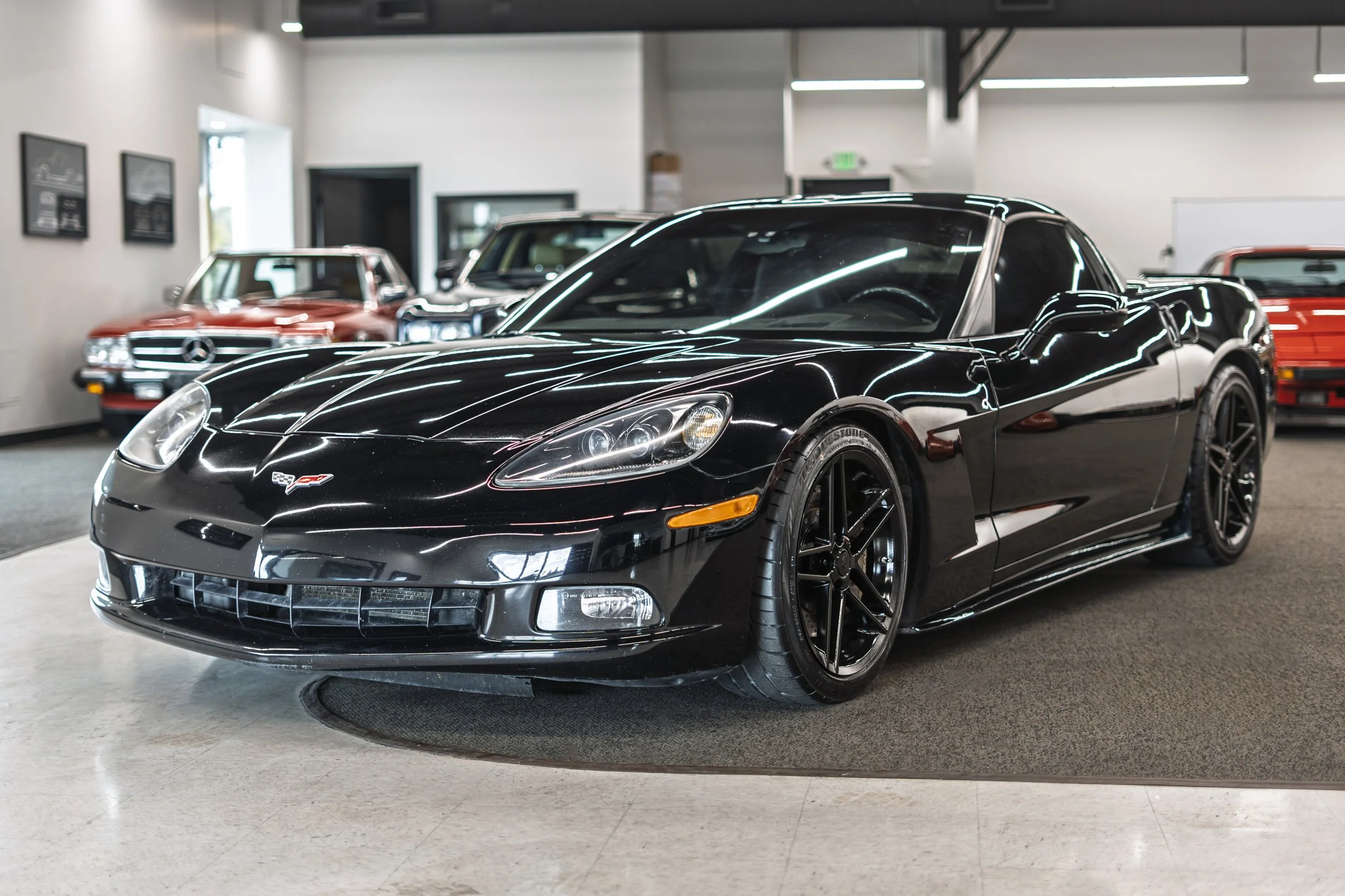 Black Chevrolet Corvette sports car inside a showroom with vintage cars in the background.