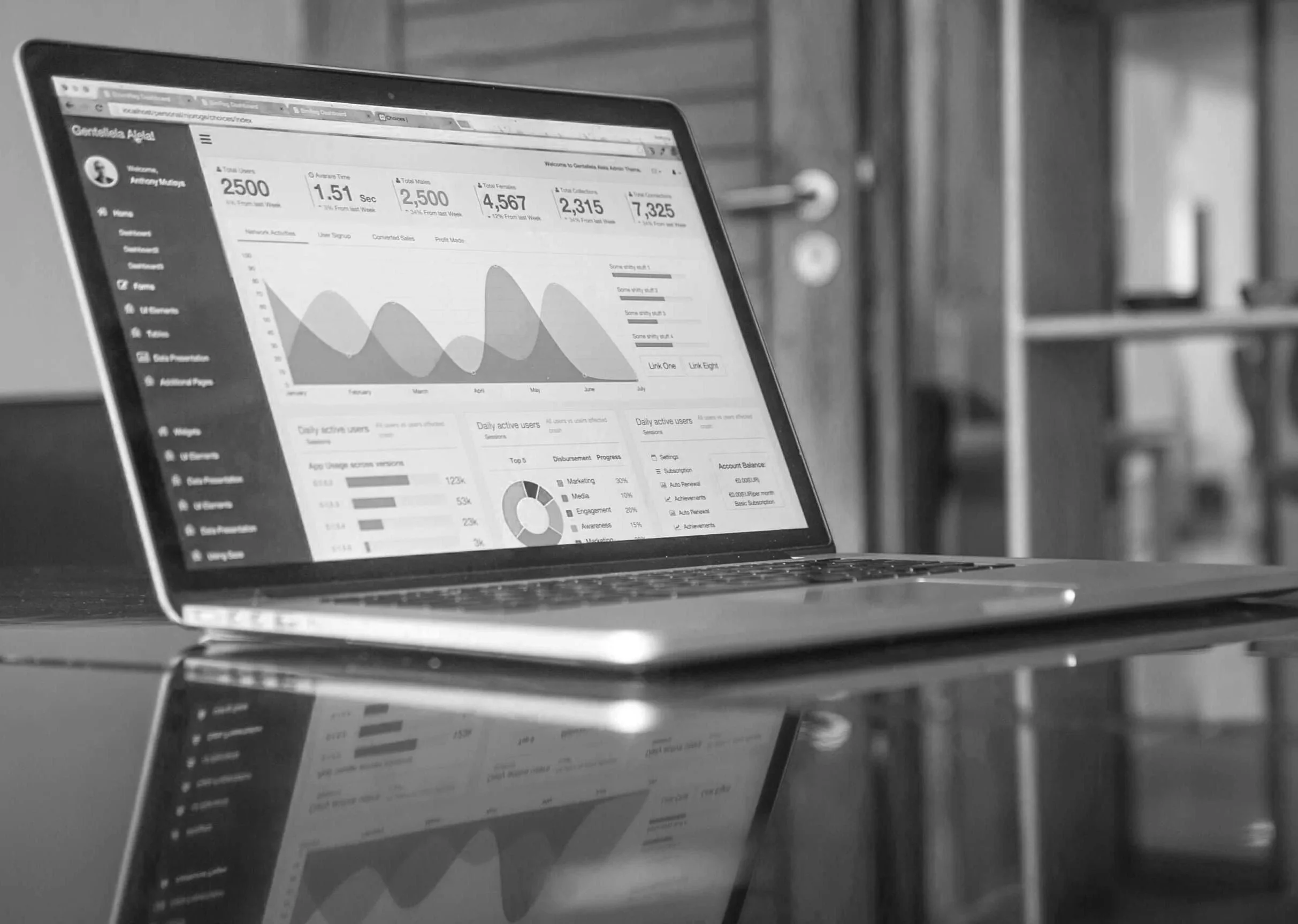 A laptop displaying analytics dashboards with graphs, numbers, and menu options on the screen, placed on a reflective surface.