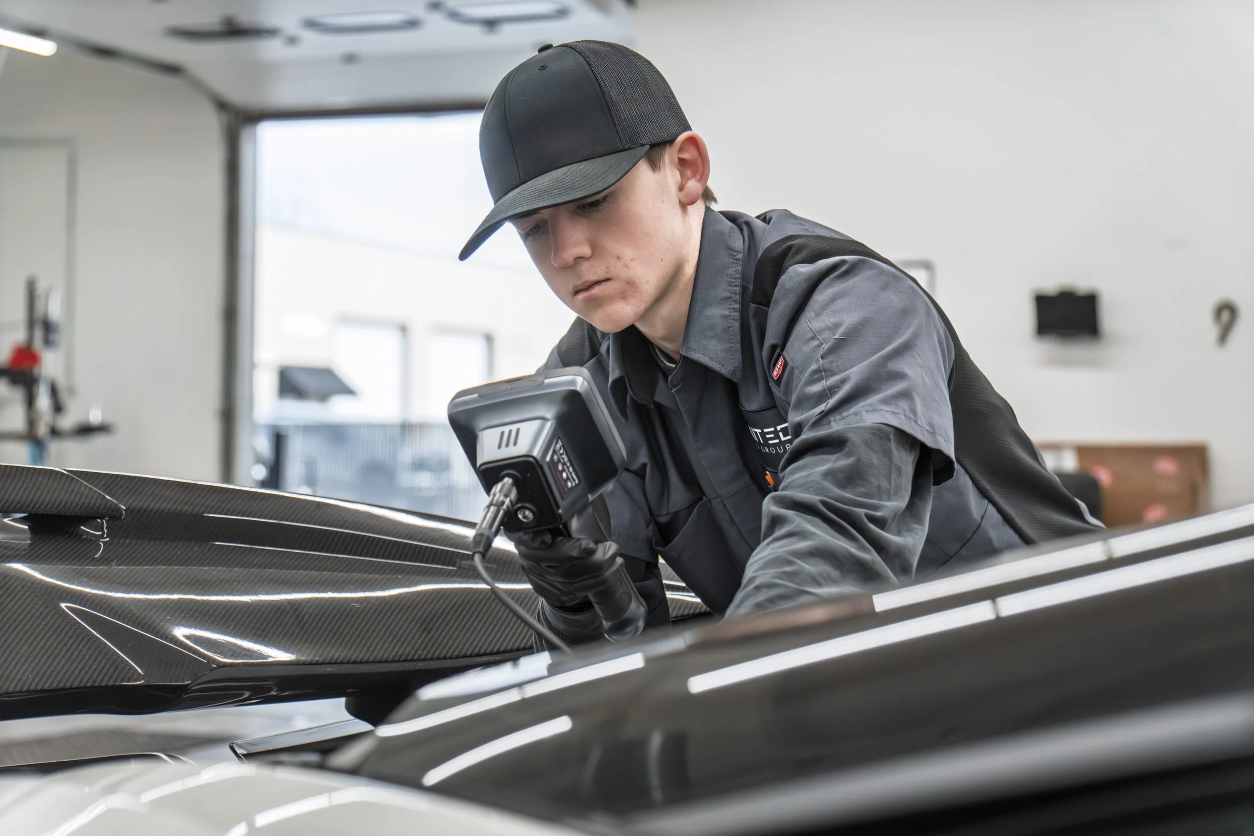 A technician in a workshop using a handheld device to inspect a black carbon fiber sports car.