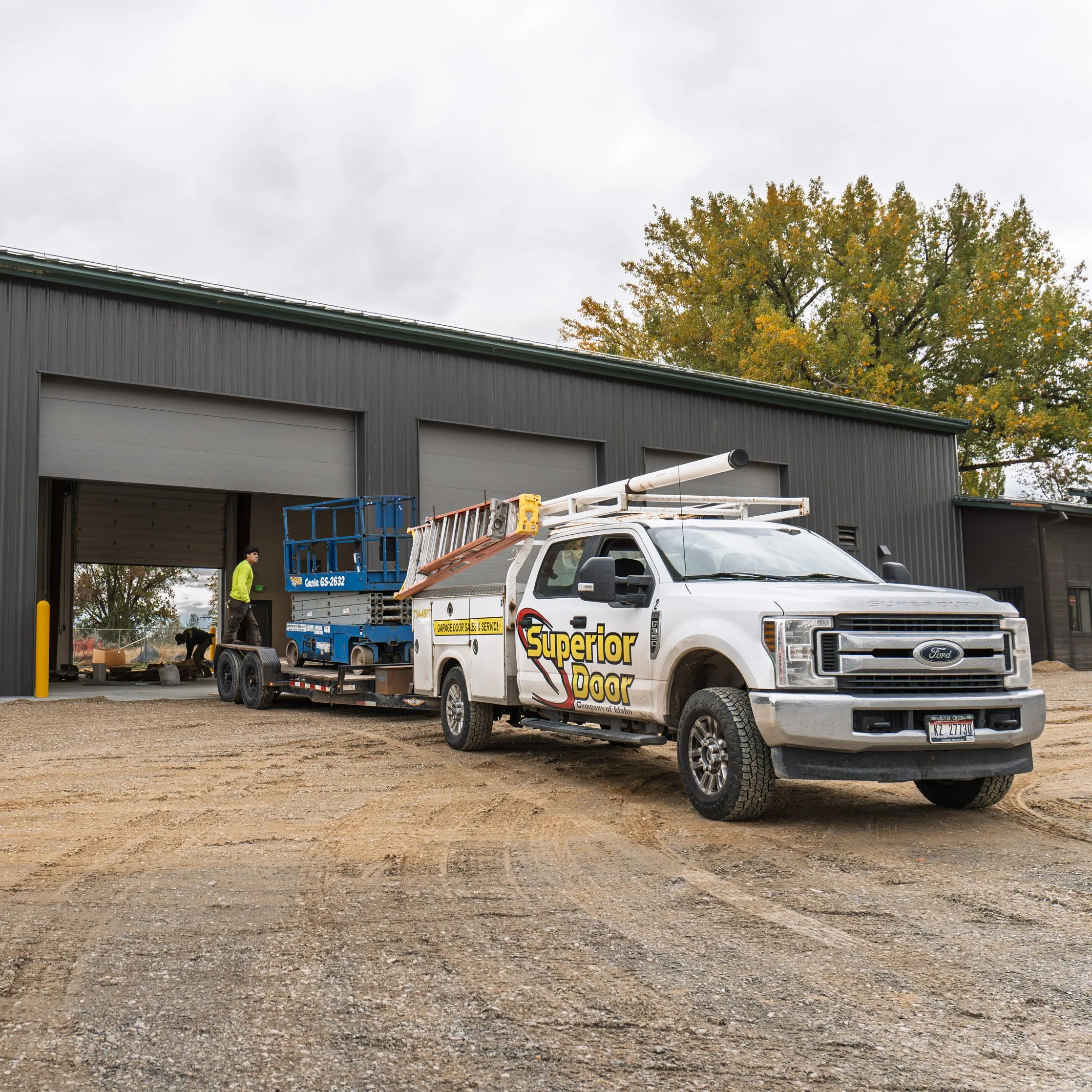 Utility truck labeled 'Superior Door' parked outside a commercial building with large garage doors, with workers unloading equipment.