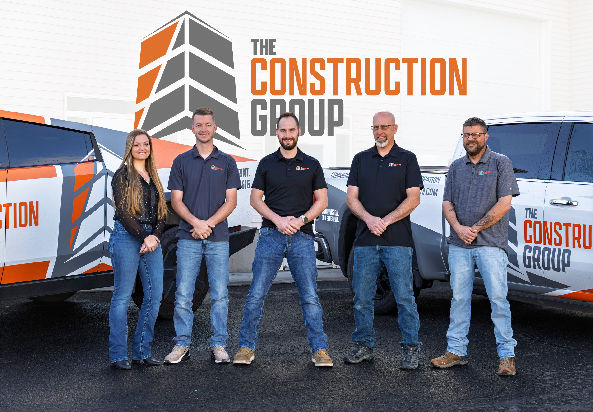 Group of five construction professionals standing in front of trucks with 'The Construction Group' branding, smiling at the camera.