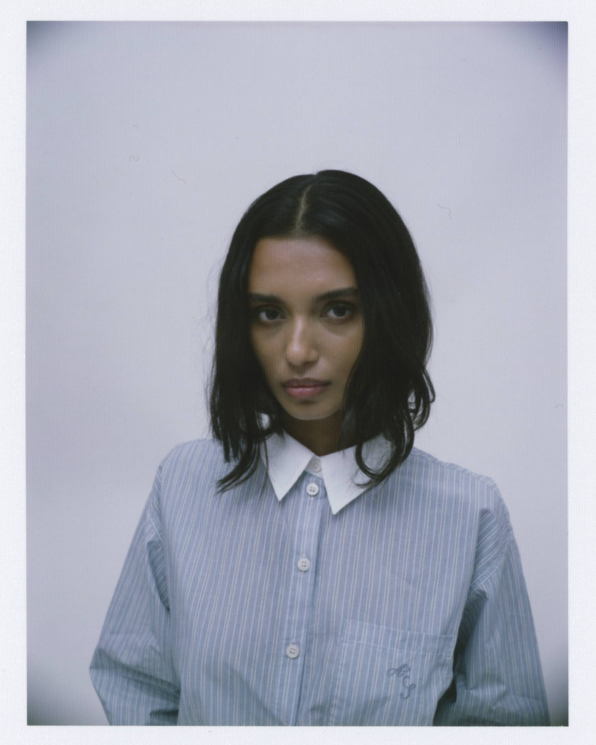 Portrait of a woman with shoulder-length dark hair wearing a blue and white striped button-up shirt against a plain light background.