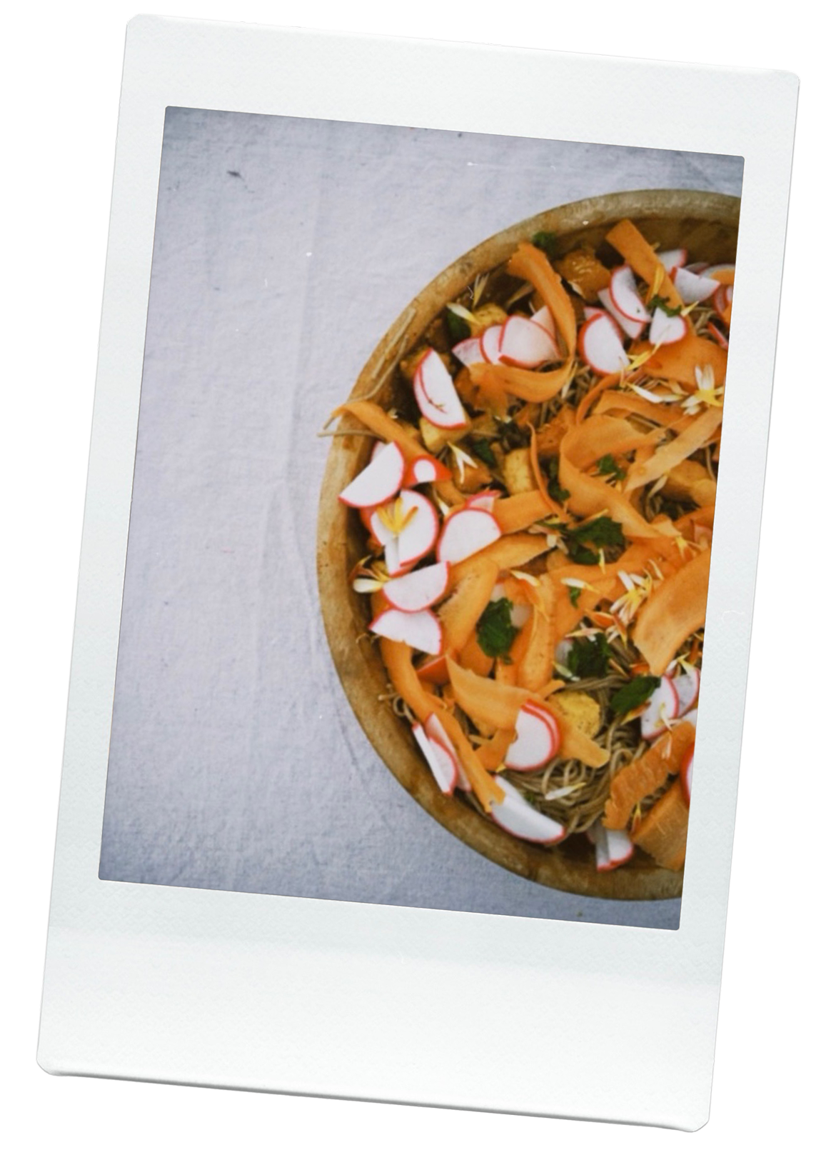 A salad topped with sliced radishes, shredded carrots, fresh herbs, and edible flowers.