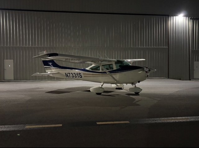 Small trimotor airplane parked on airport tarmac at night.