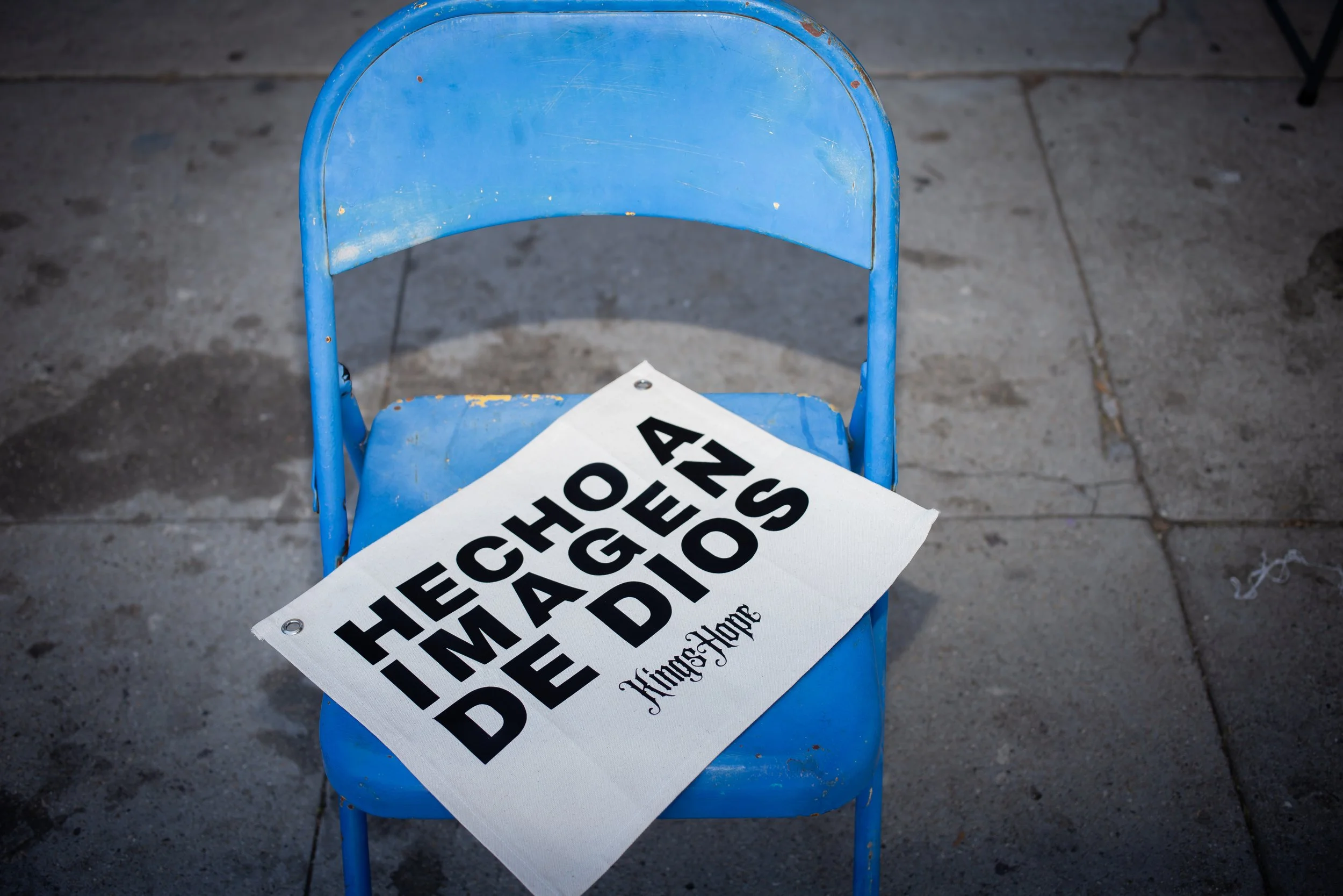 KingsHope Hecho A Imagen De Dios canvas banner resting on blue folding chair on sidewalk