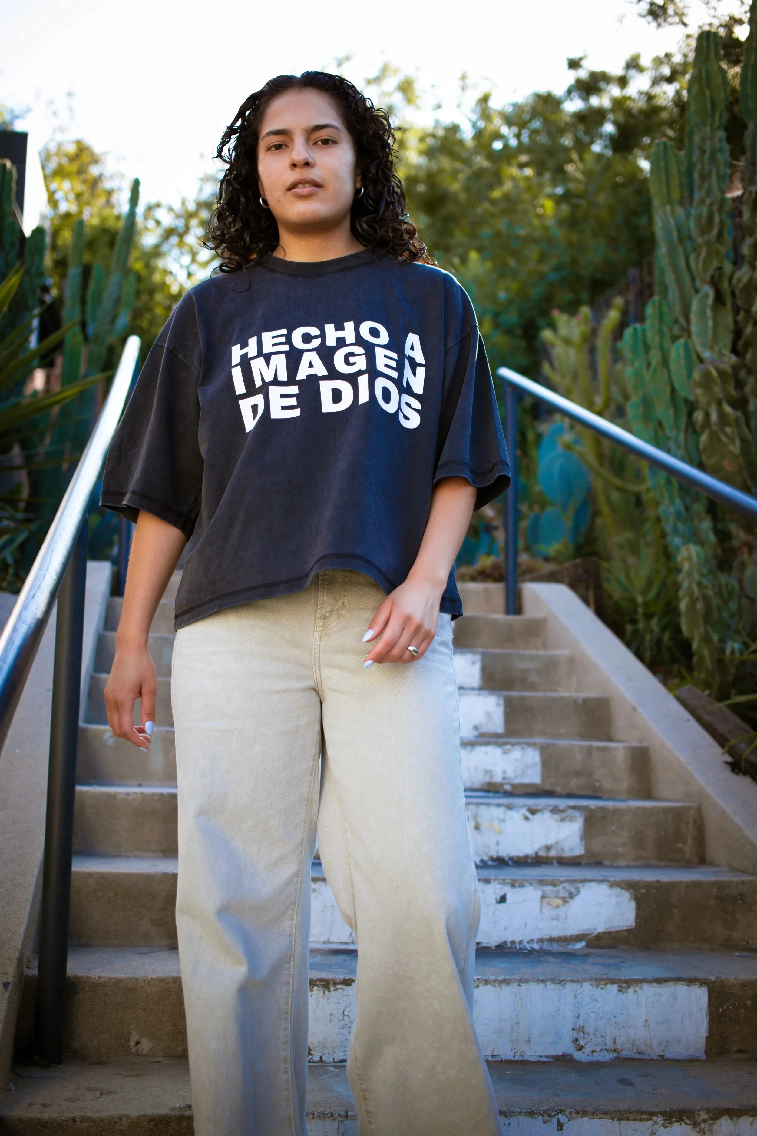 Woman wearing KingsHope Hecho crop tee in washed charcoal on concrete staircase with cacti
