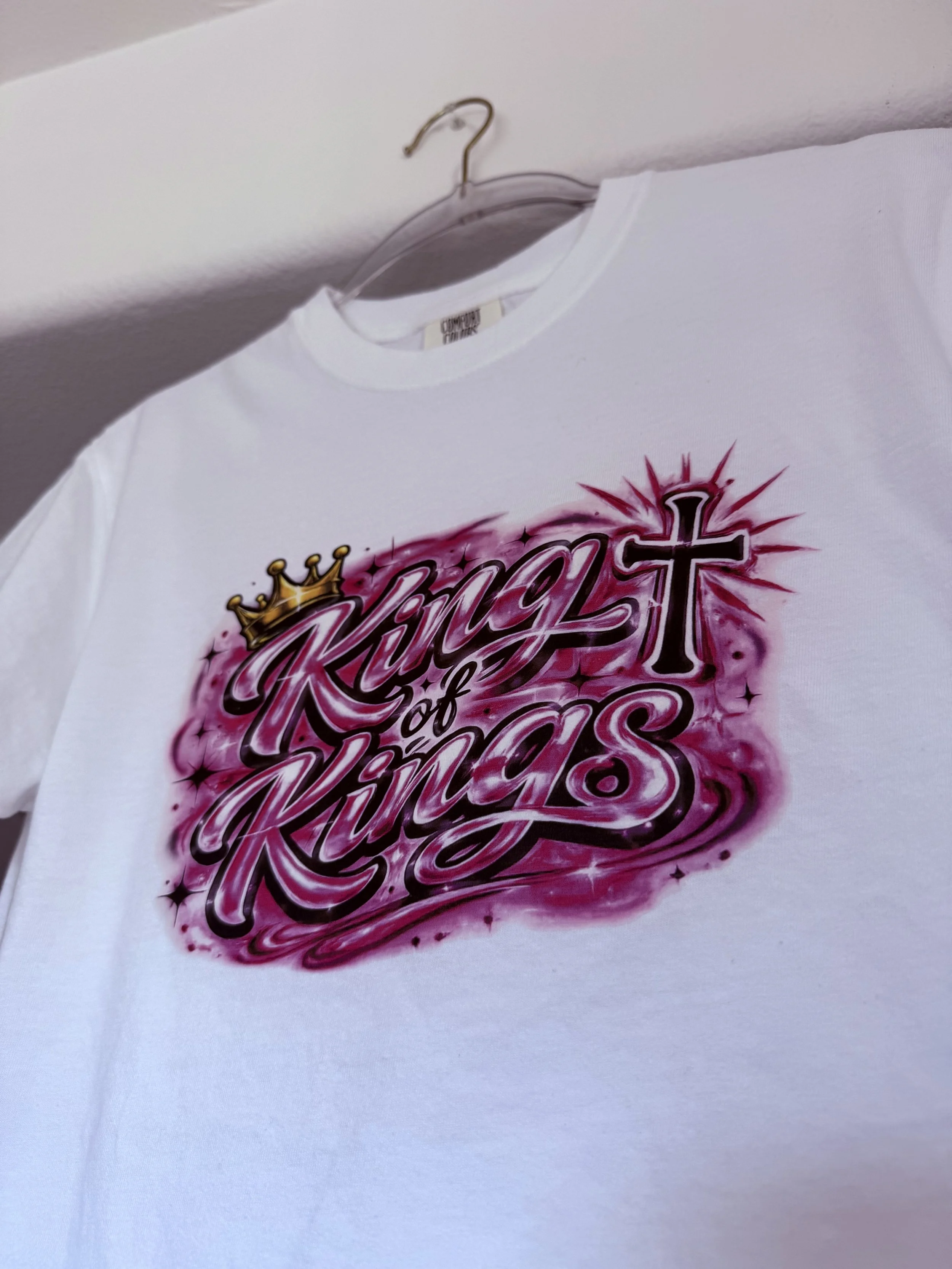 KingsHope King of Kings tee in pink airbrush print hanging on hanger, Comfort Colors white tee