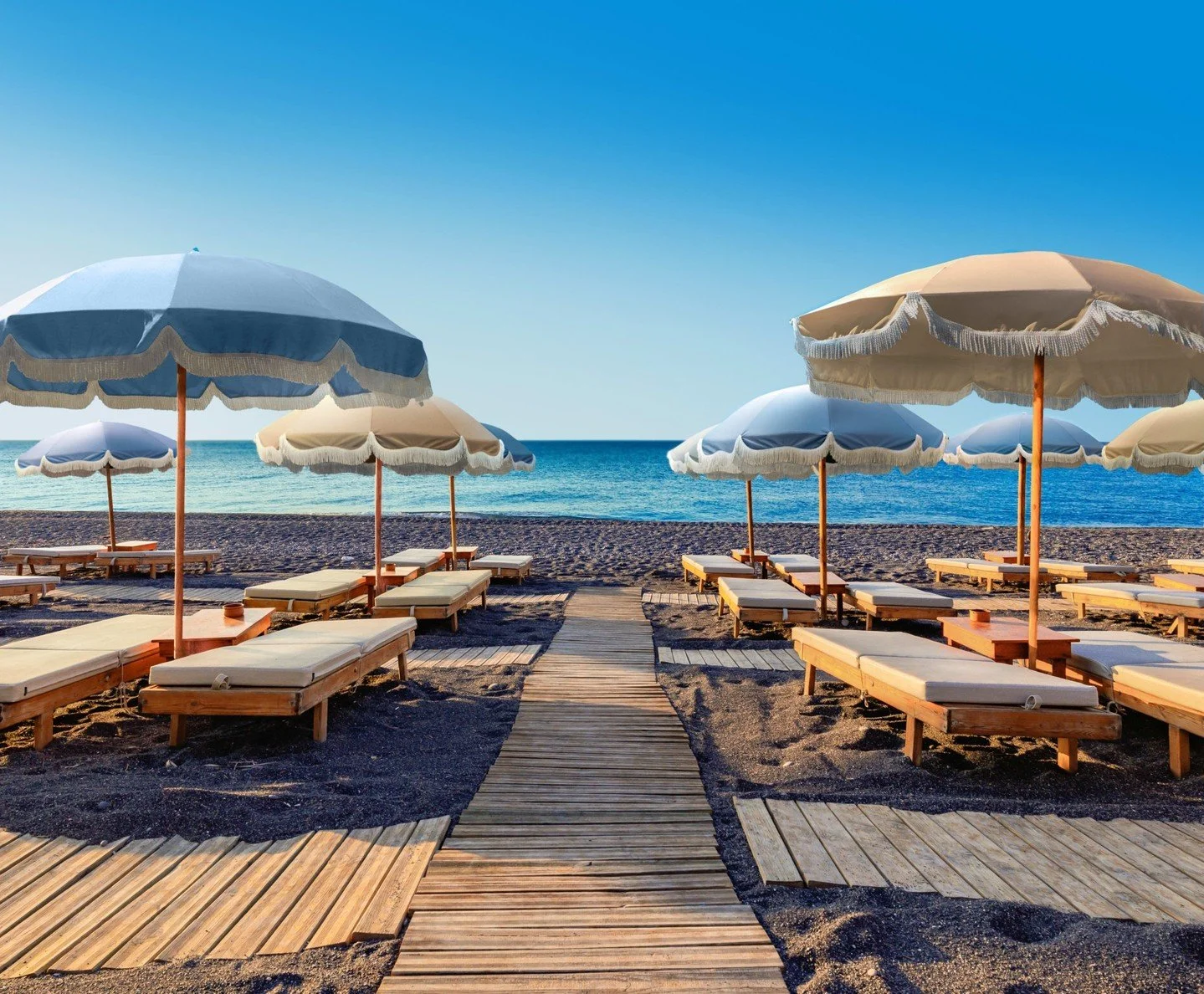 Plush towels, shaded loungers, and breathtaking views from a secluded black‑sand beach&hellip; this is relaxation redefined at Royal Beach Club Santorini 🌅💙

Make this your next getaway &mdash; message me at jessica@bookedandboundless.com today to 