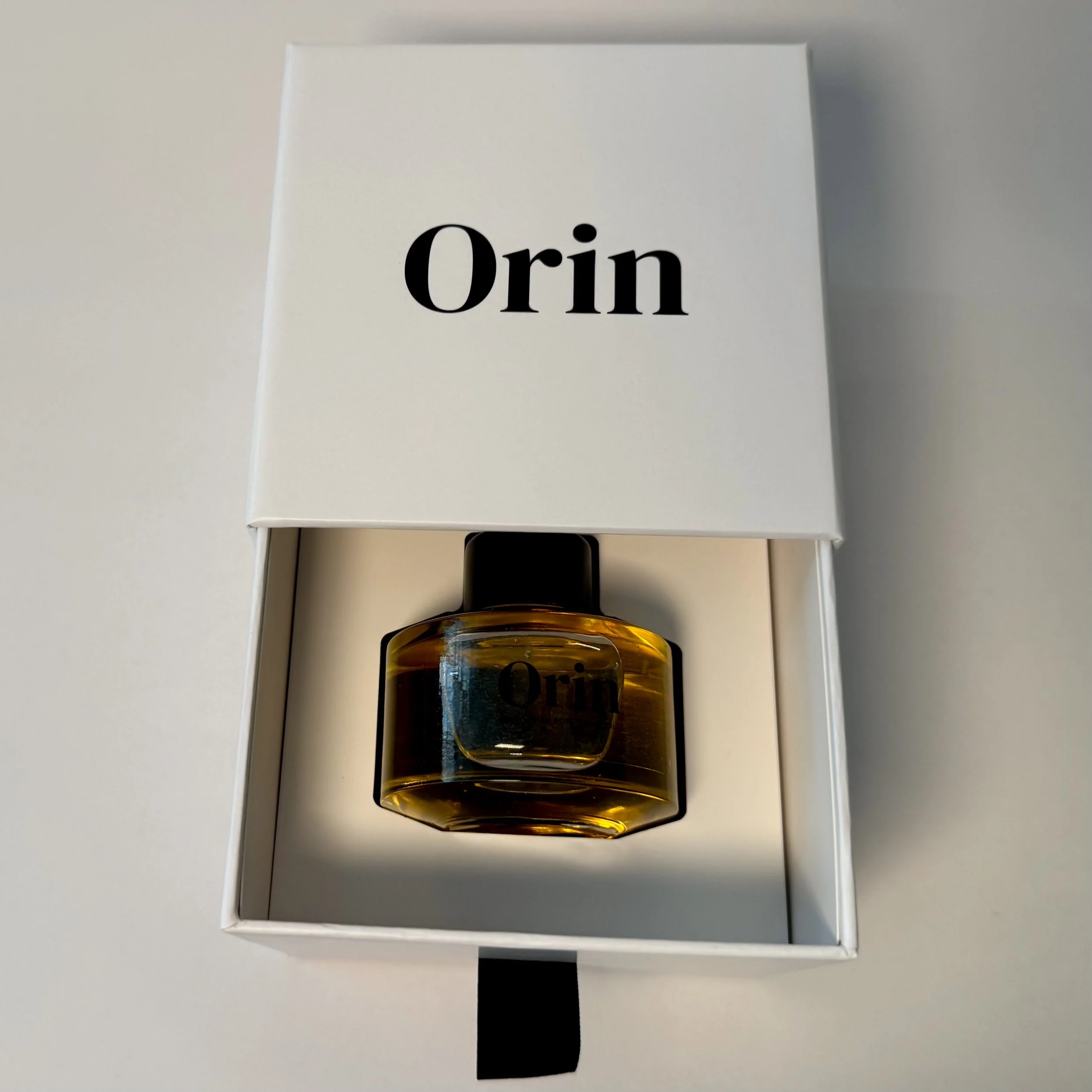Top-down view of 50ml Orin Bulgarian Rose Body Oil in an open white luxury skincare box. The golden liquid reflects the receptive, structural nourishment of this high-performance botanical ritual.