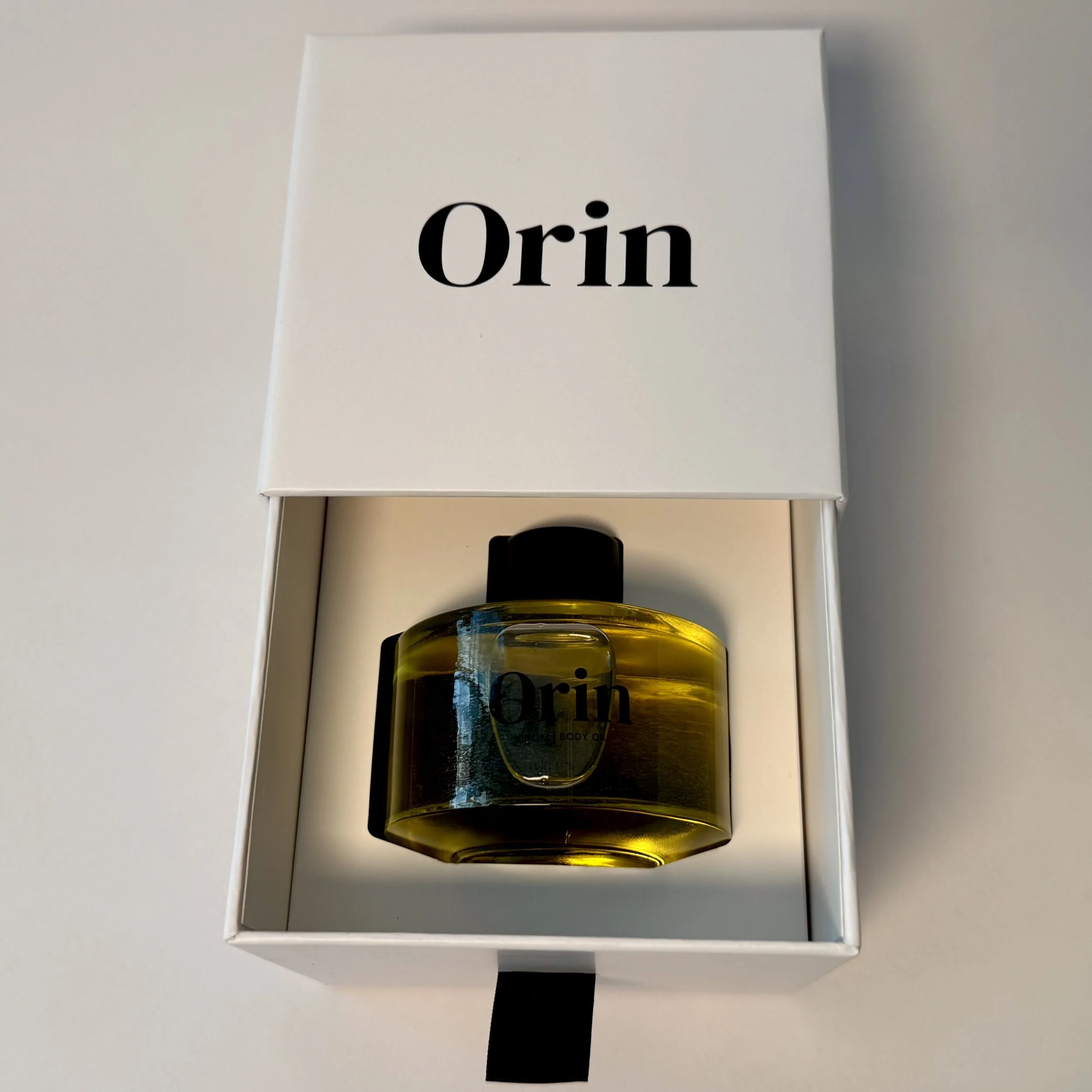 100ml Orin Hinoki Body Oil nestled in an open white luxury drawer box. This premium presentation showcases the grounding botanical oil, formulated for deep barrier nourishment and stability.