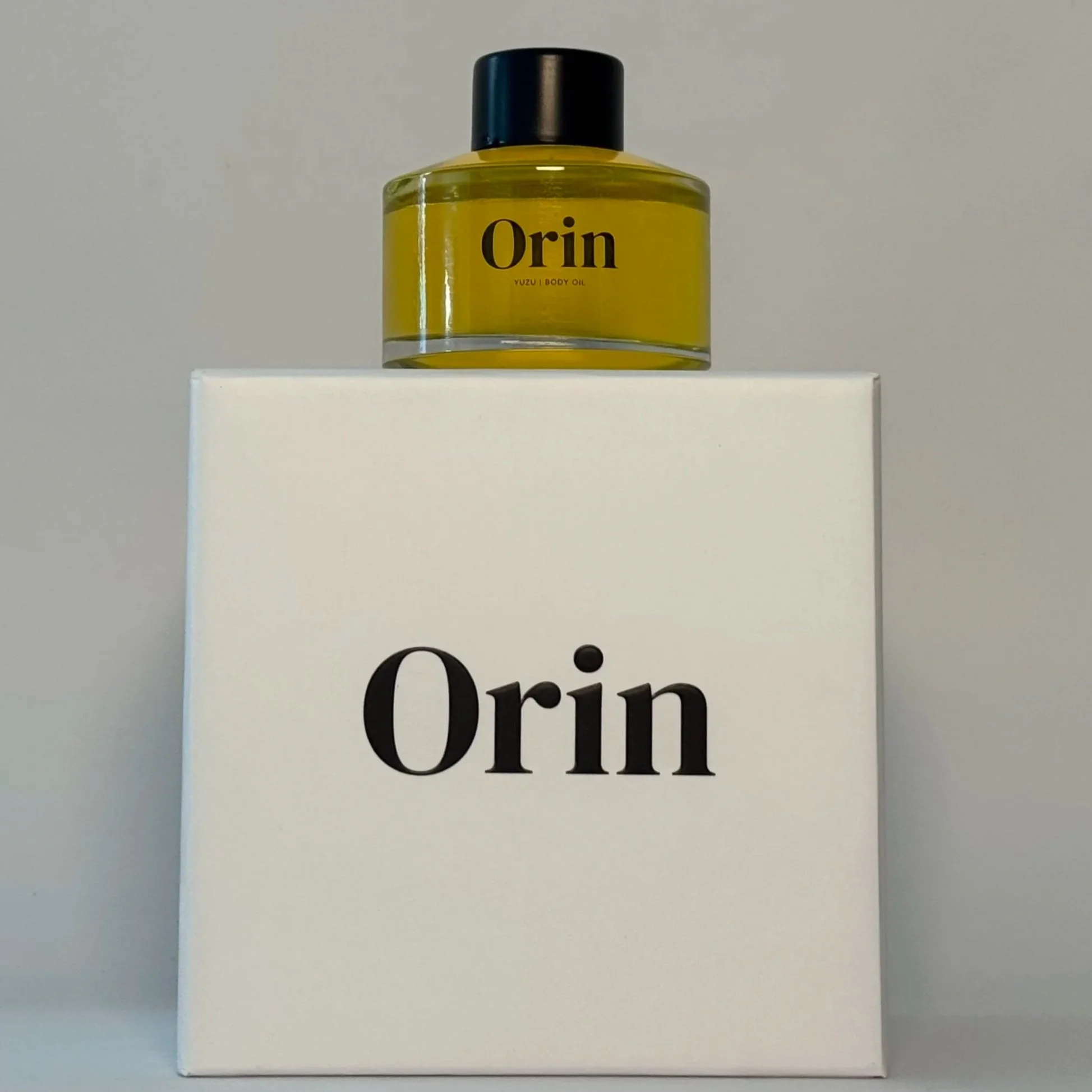 50ml glass bottle of Orin Yuzu Body Oil on a white packaging box. With its black cap, this antioxidant-rich botanical skincare formula awakens natural radiance and smooths skin texture appearance.