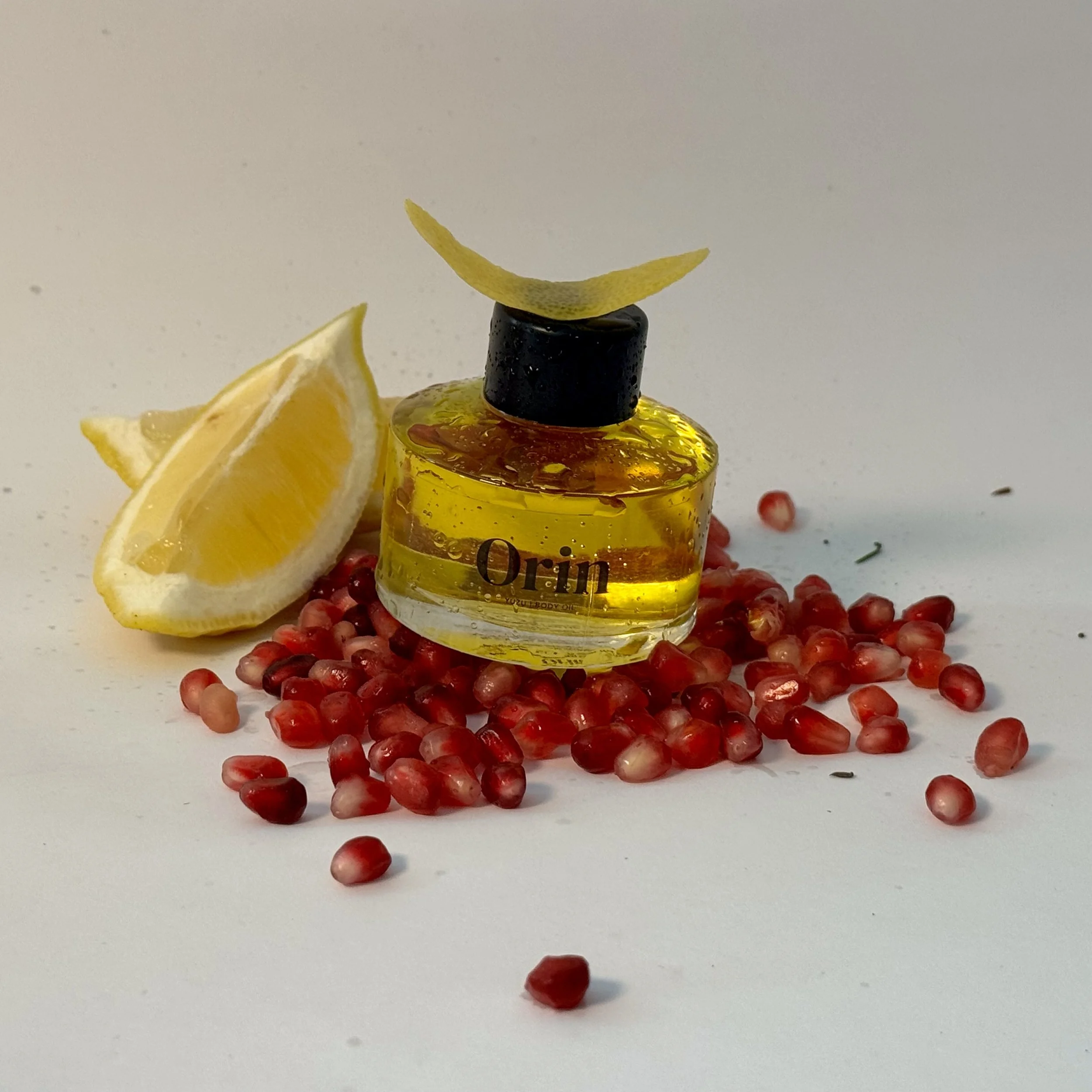 Orin Yuzu Body Oil styled with fresh pomegranate seeds and citrus wedges. This vibrant scene highlights the formula's antioxidant-rich botanical ingredients designed for a visibly even complexion.