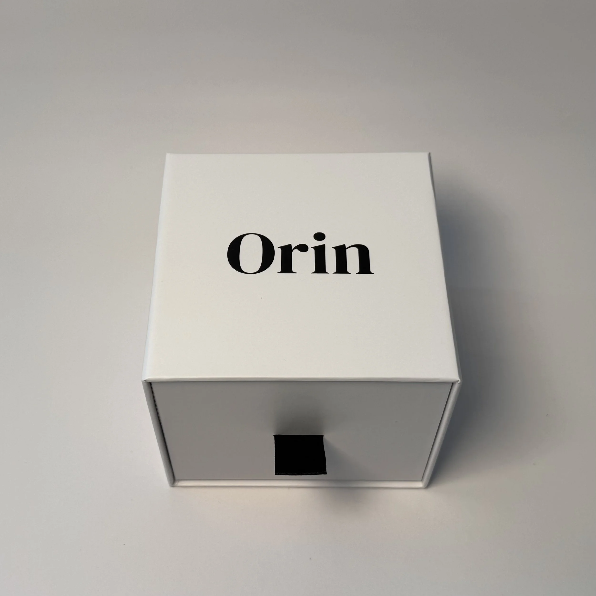 Closed white Orin luxury skincare box with a black logo and ribbon tab. This elegant packaging houses the Yuzu botanical body oil collection for elevated daily rituals.